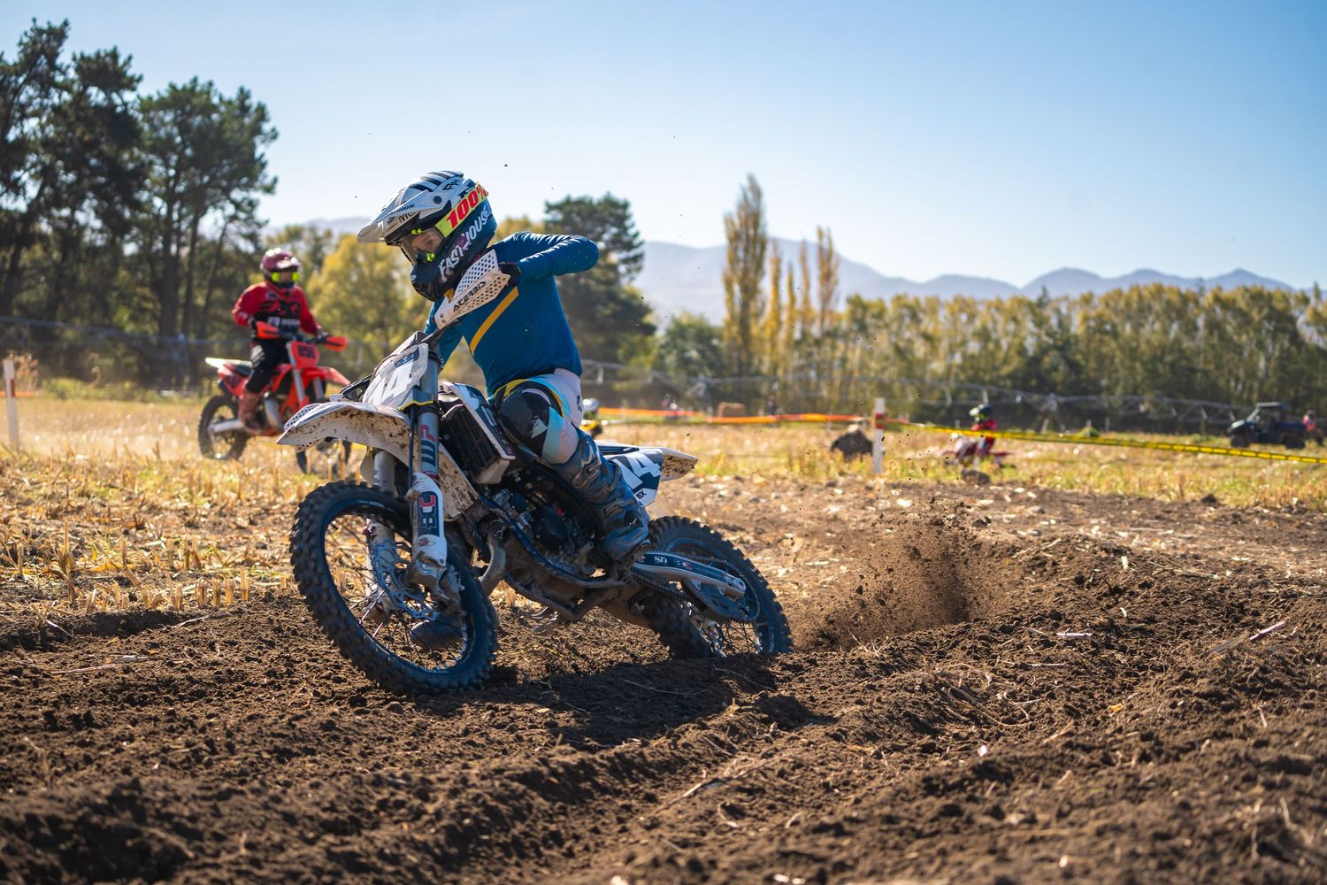 Dirt bikes racing through a dusty motocross track with trees and mountains in the background at a funday in North Canterbury.