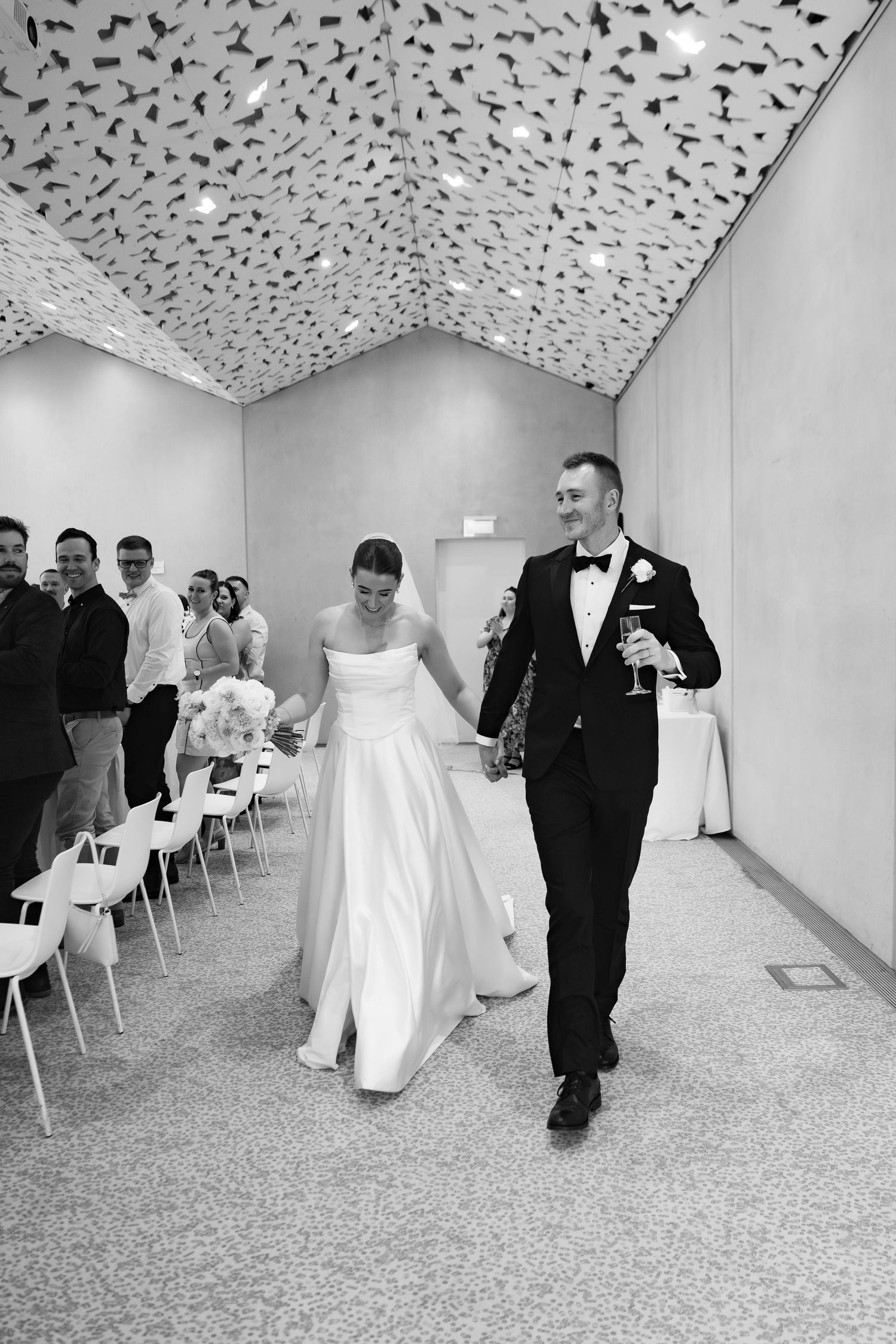 Black and white photo of a smiling bride and groom holding hands walking into their wedding reception at ilex cafe.