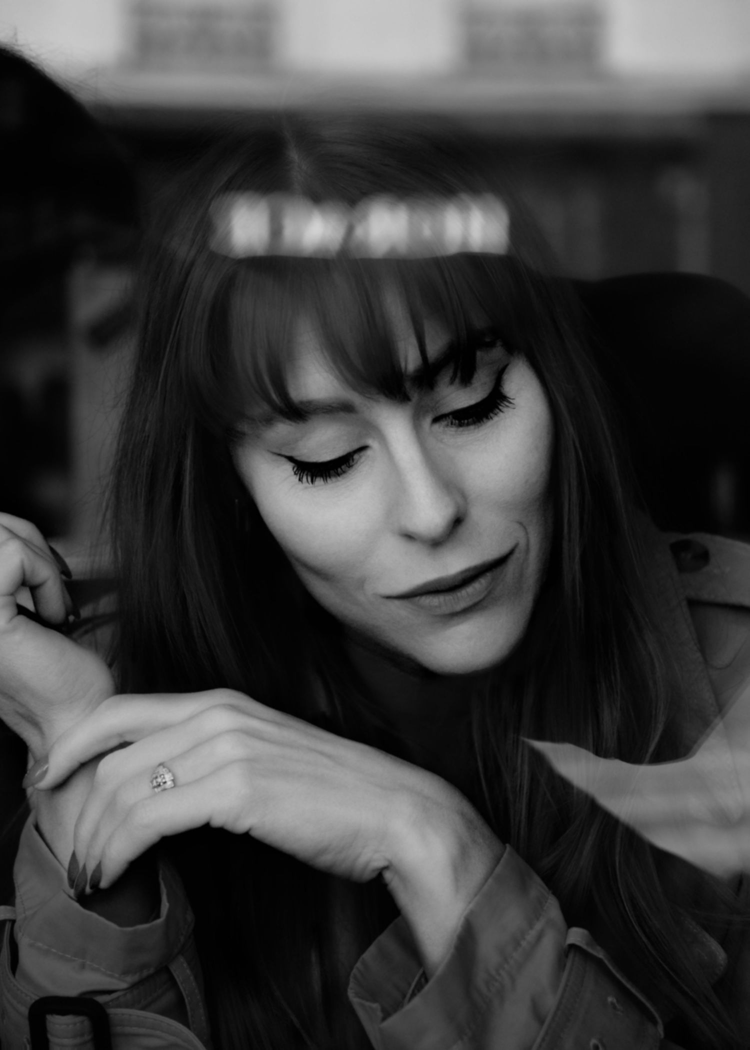 Black and white portrait of a woman with long dark hair and bangs looking down pensively while resting her chin on her hand.