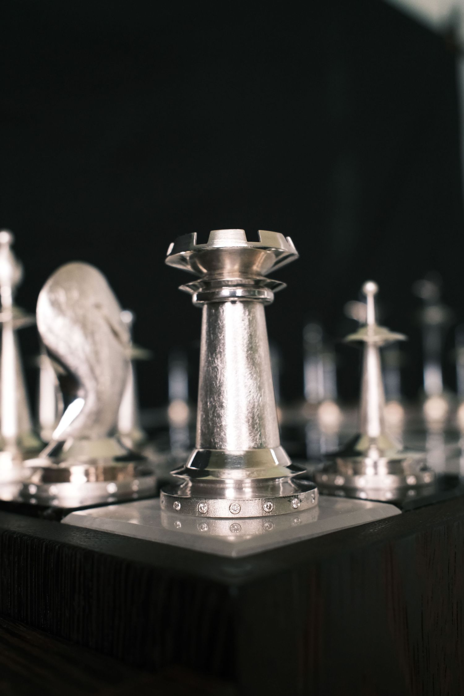 Close-up view of metallic chess pieces on a dark board showing reflective surfaces and dramatic lighting.