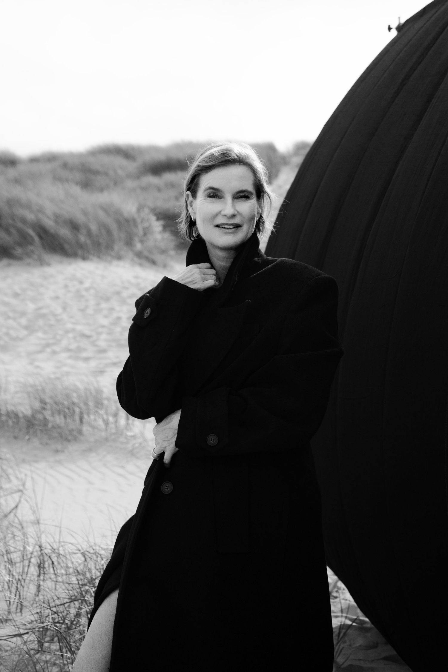 A black and white photo series of people walking along a beach with windswept hair and dark coats.