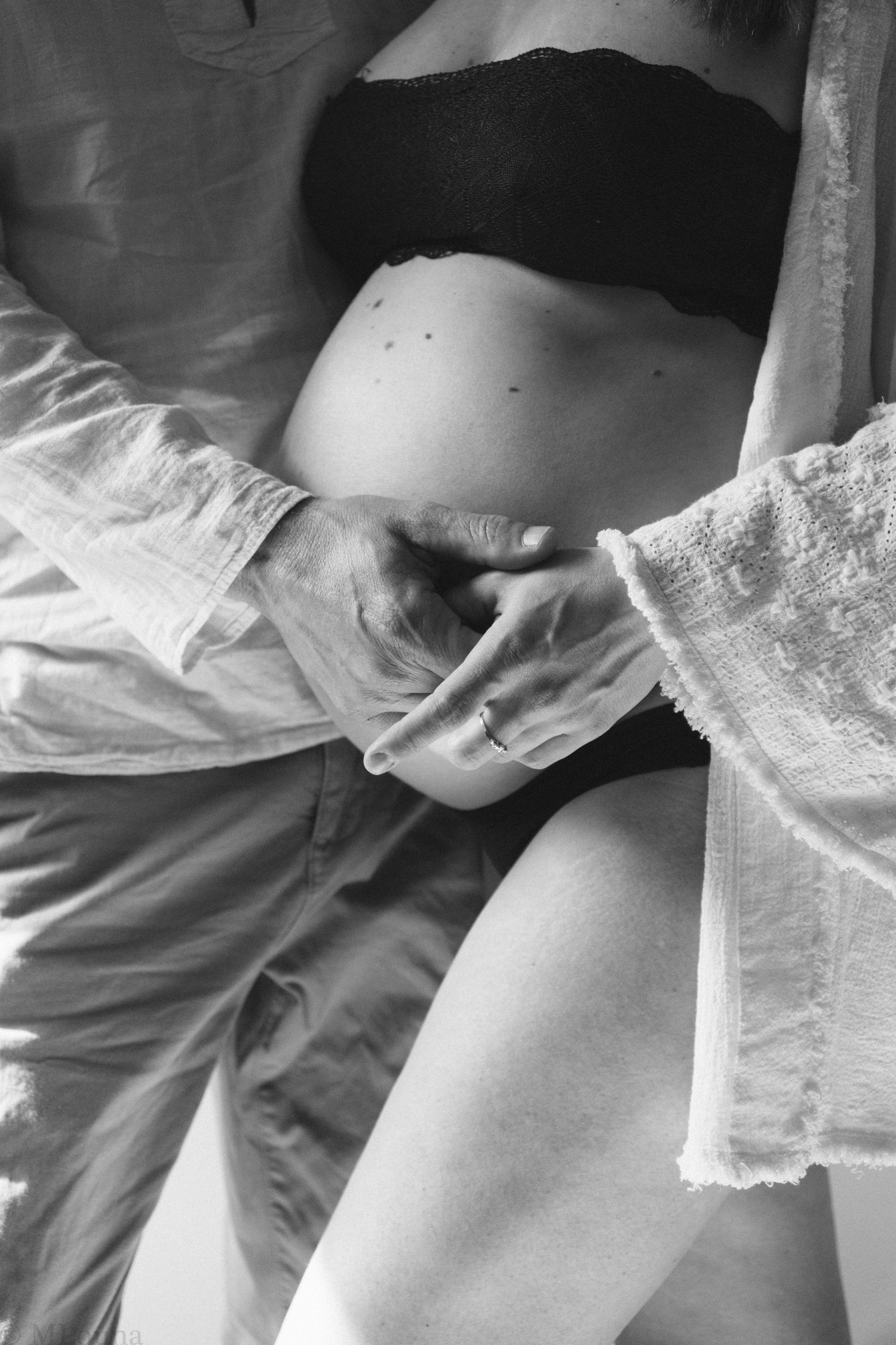 A black and white image shows a person putting on a delicate lace garter belt around their leg.