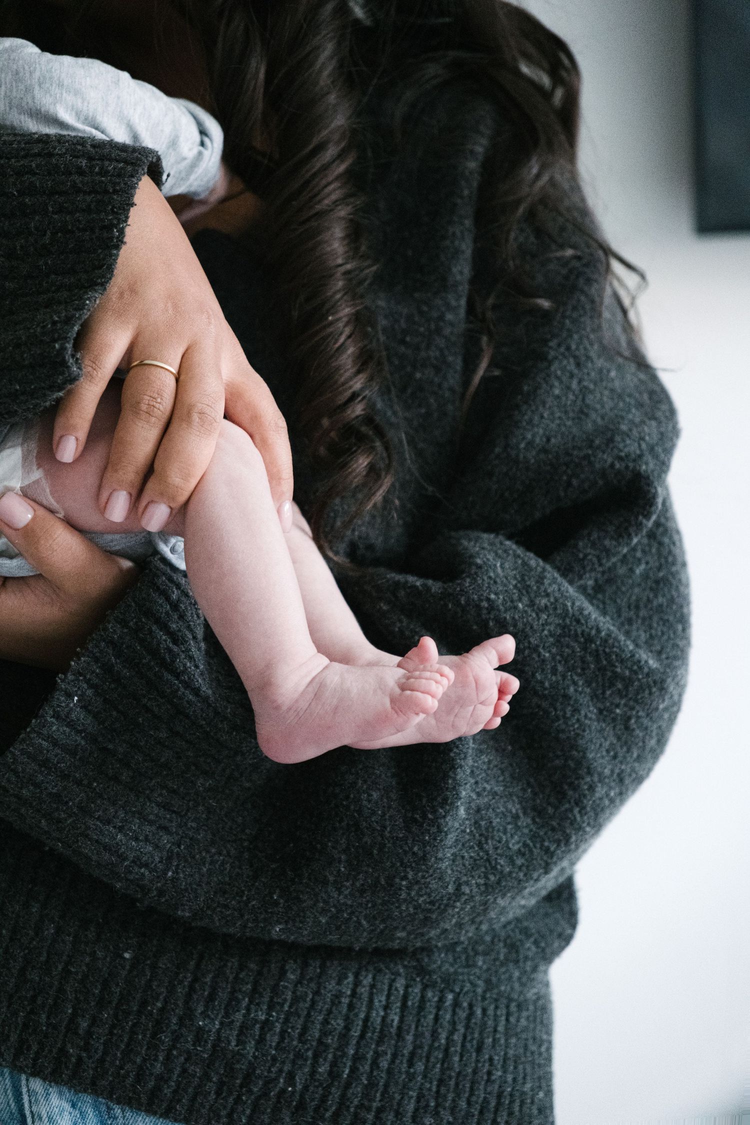 A series of photos showing hands cradling a baby's bare feet against a dark gray sweater background.