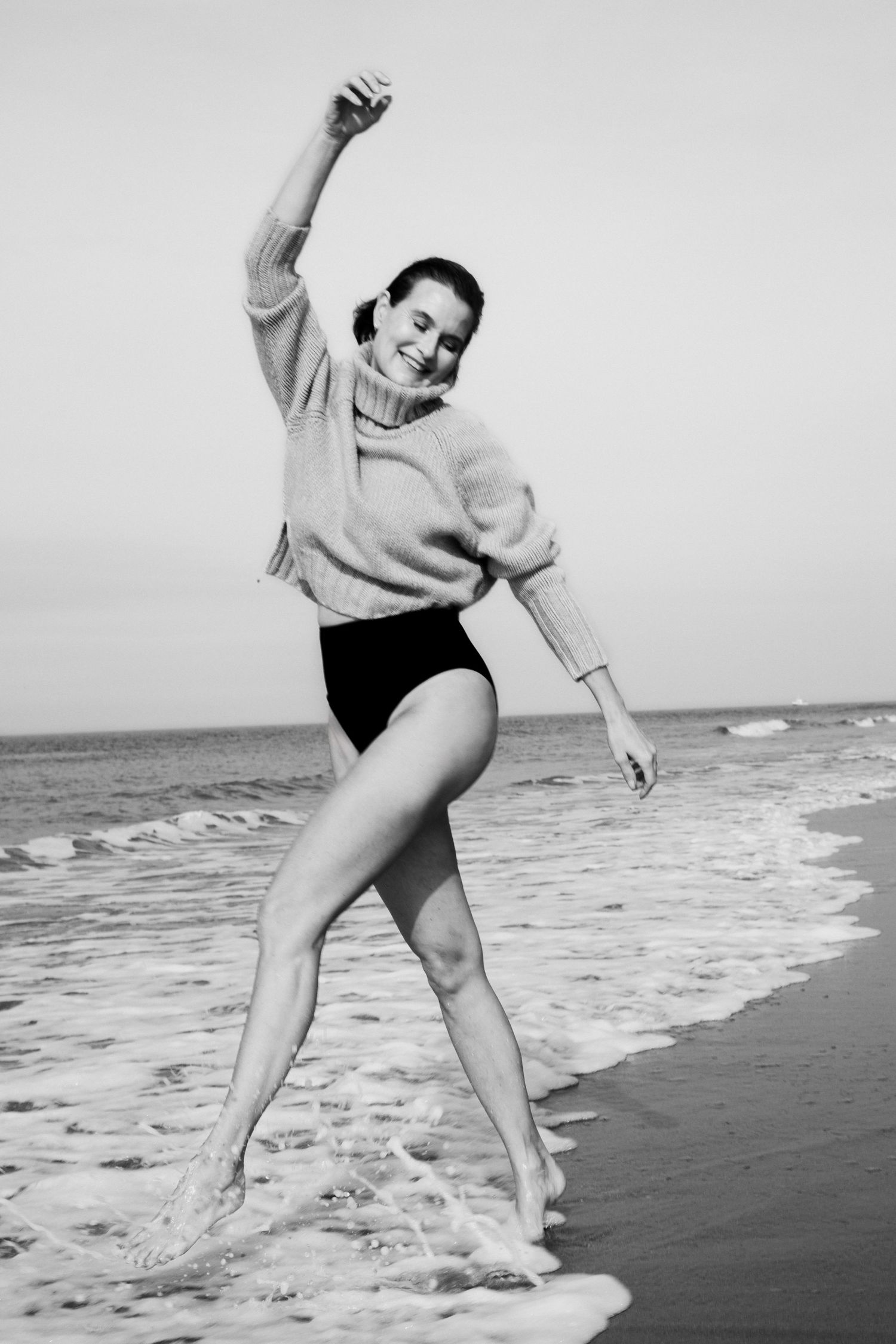 A sequence of black and white photos showing a person dancing joyfully on a beach with ocean waves in the background.