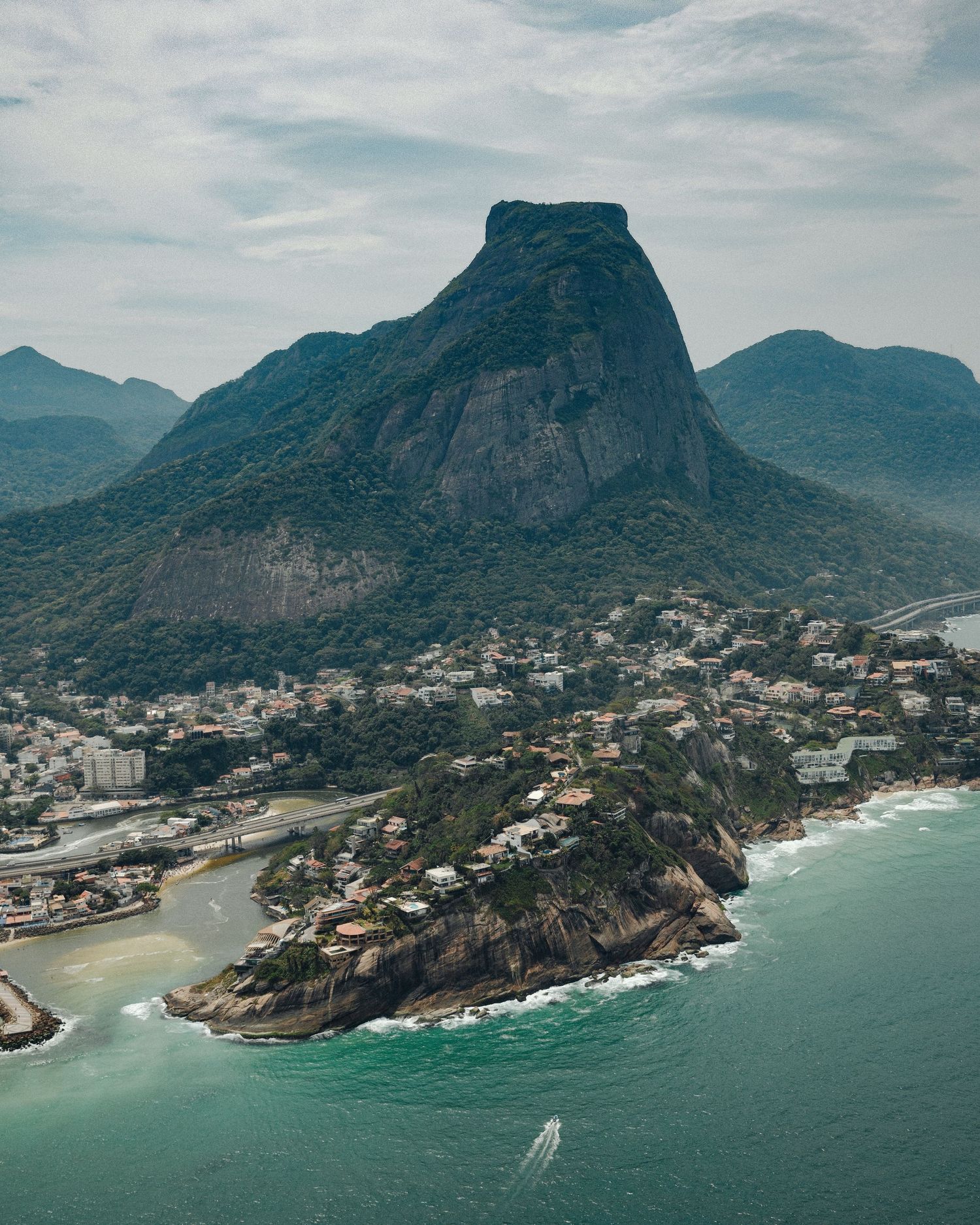 Aerial panoramic view of Rio de Janeiro's coastline with mountains, beaches, and urban development along the shore.