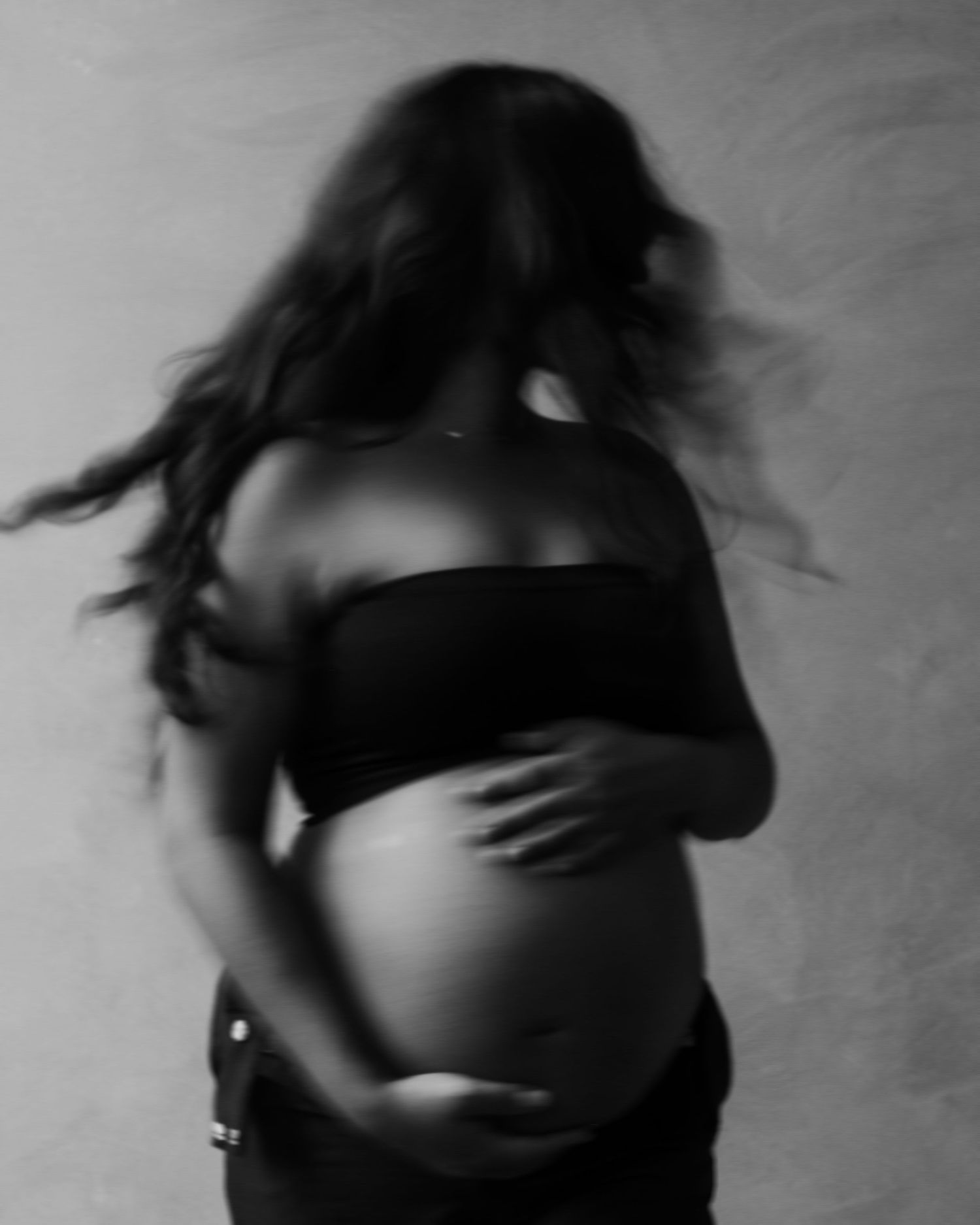 Black and white artistic maternity silhouette showing a pregnant woman in motion with flowing hair.