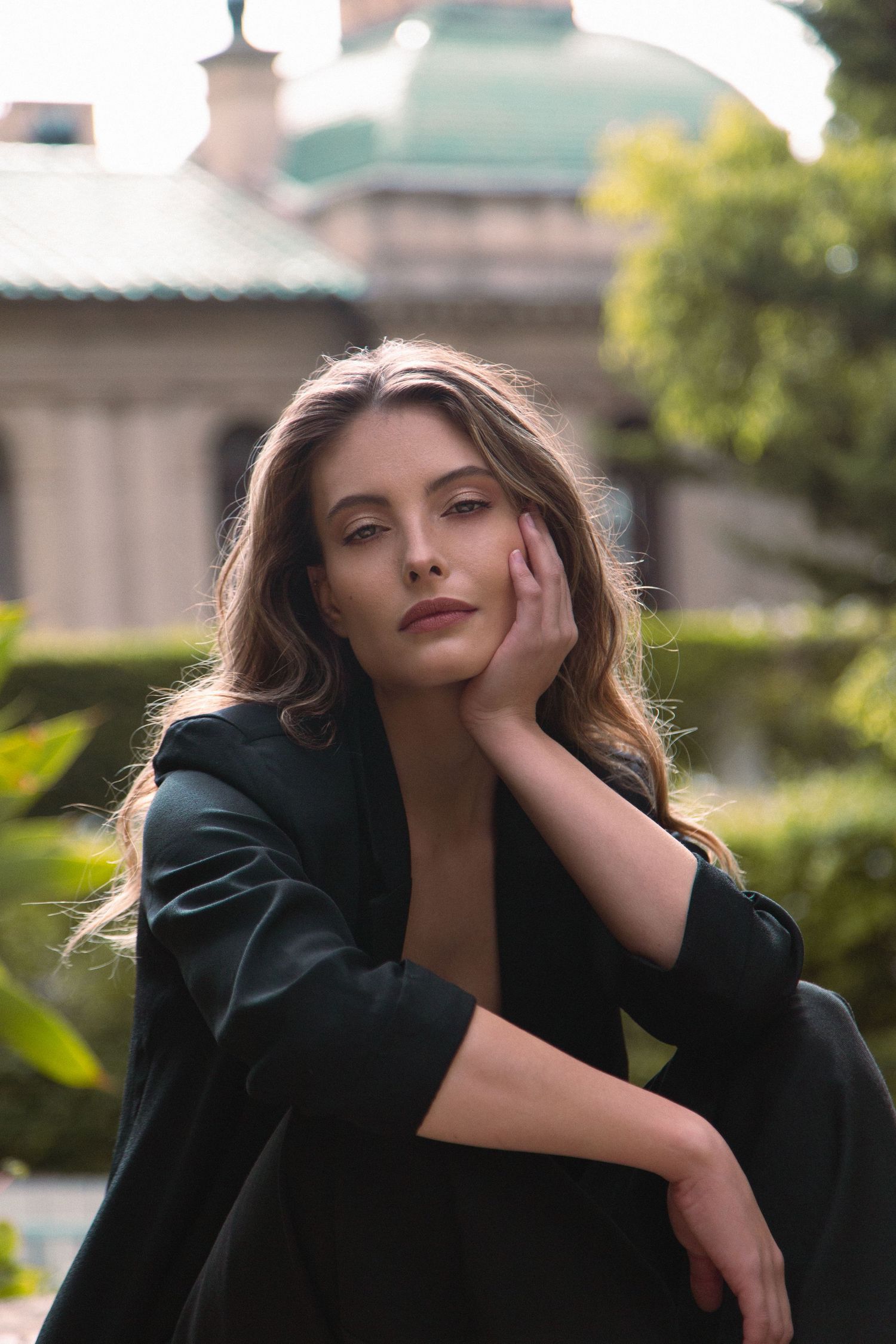 A fashion portrait series showing dramatic poses in a black outfit against a blurred outdoor background.