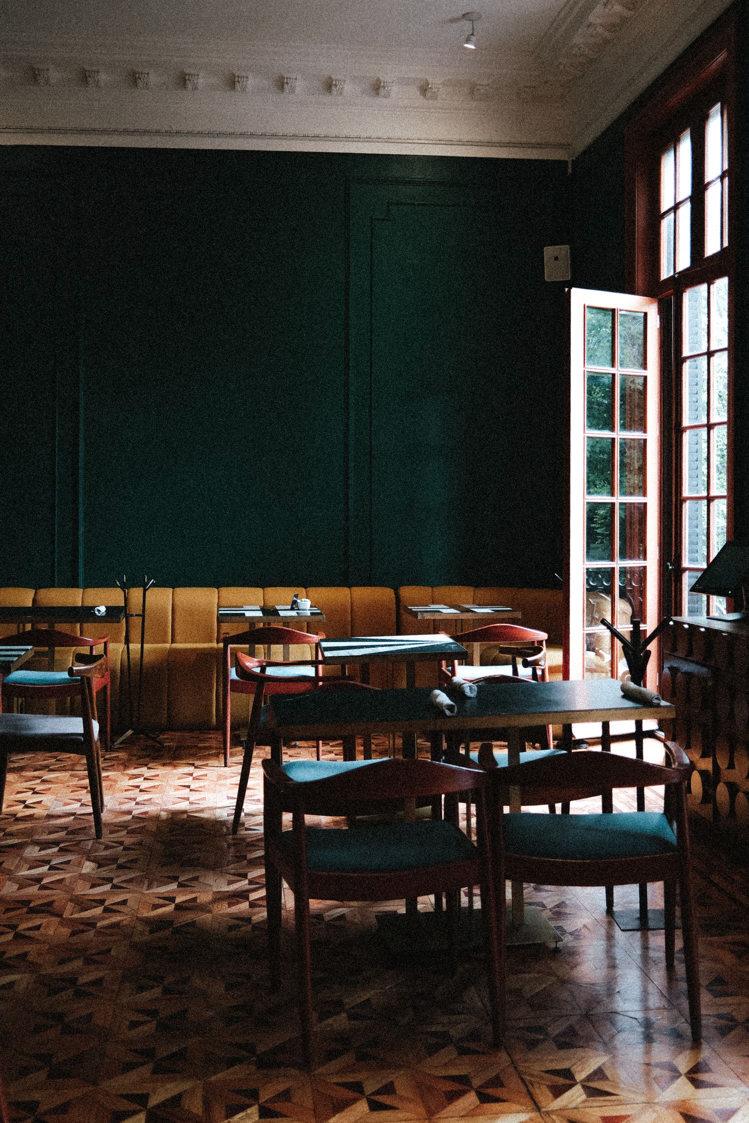 Panoramic view of an empty restaurant dining room with dark green walls and patterned carpet showing multiple tables and chairs.