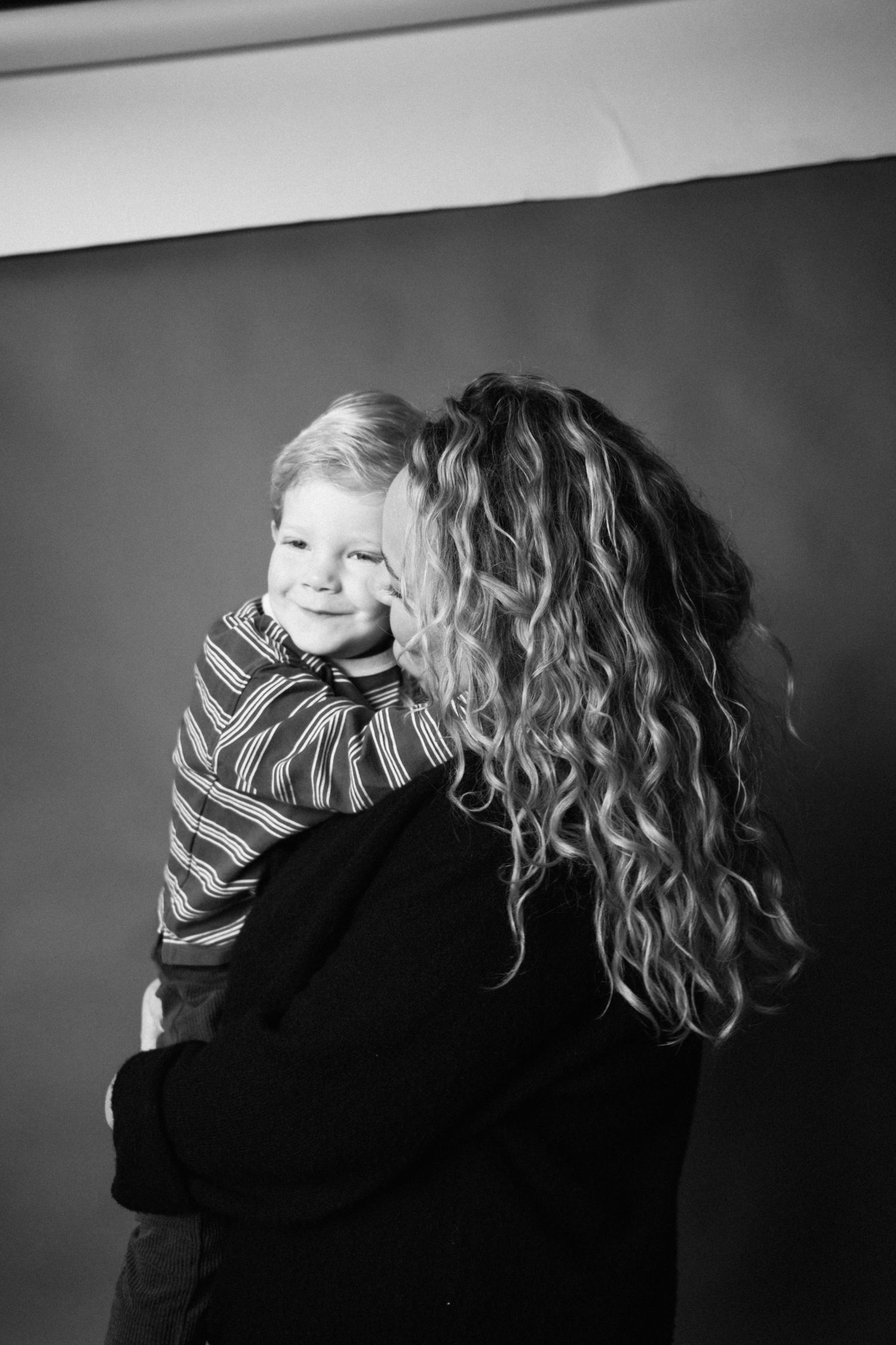 A black and white photo series showing an intimate embrace between two figures with curly hair against a dark background.