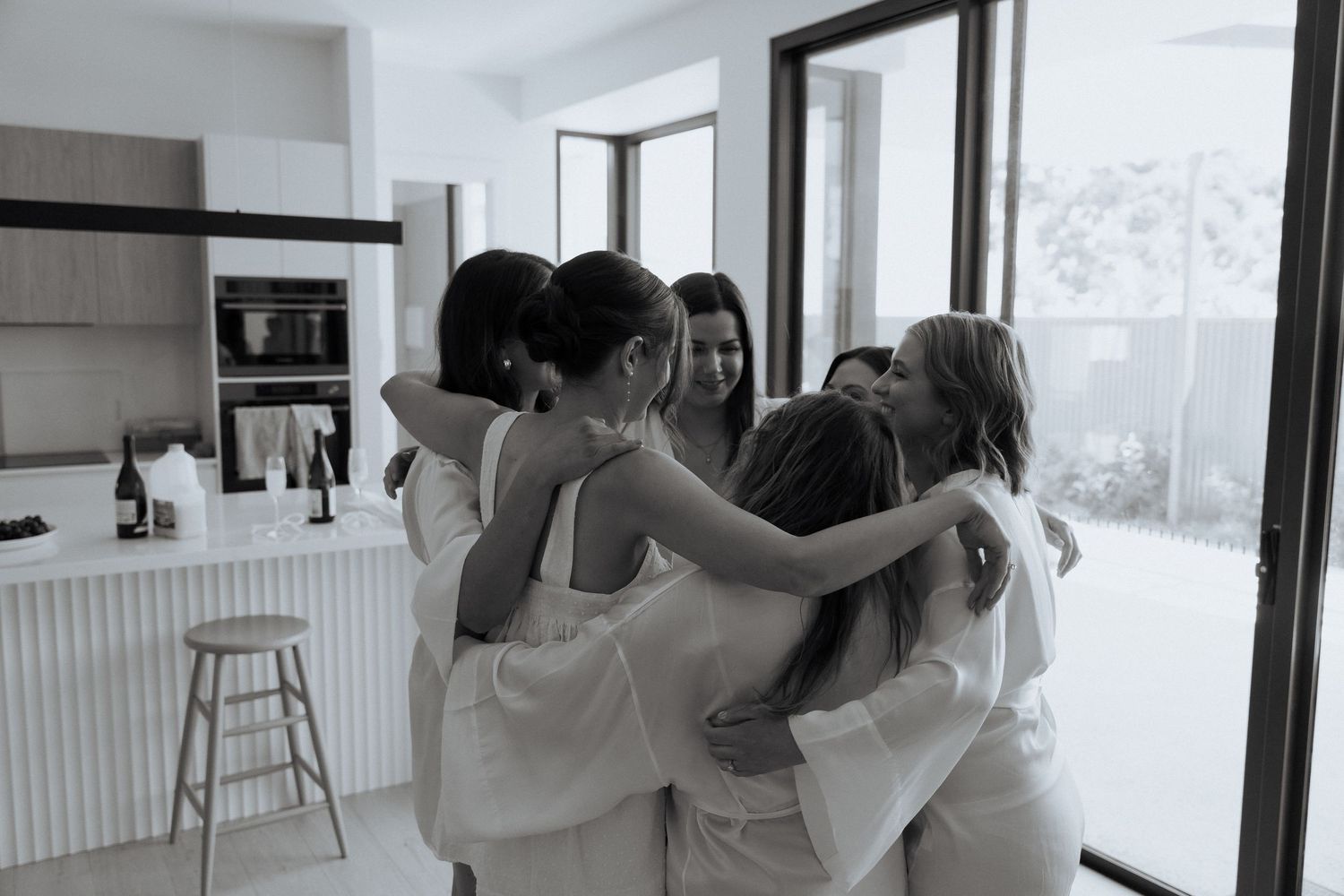 Wedding party dancing together in a bright modern room with windows.