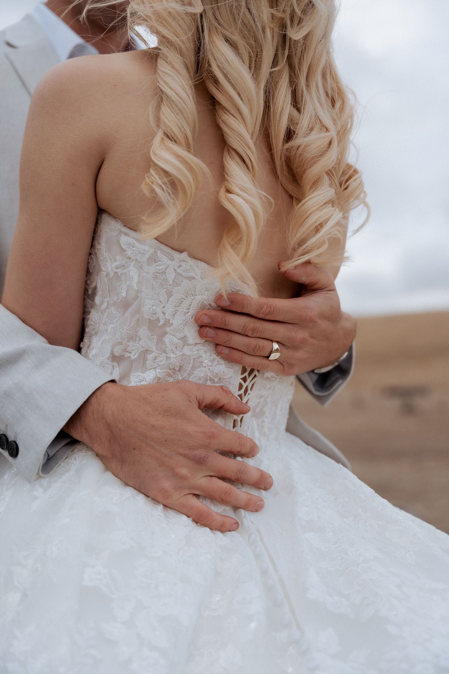 Close-up of hands with wedding rings on a lace wedding dress.