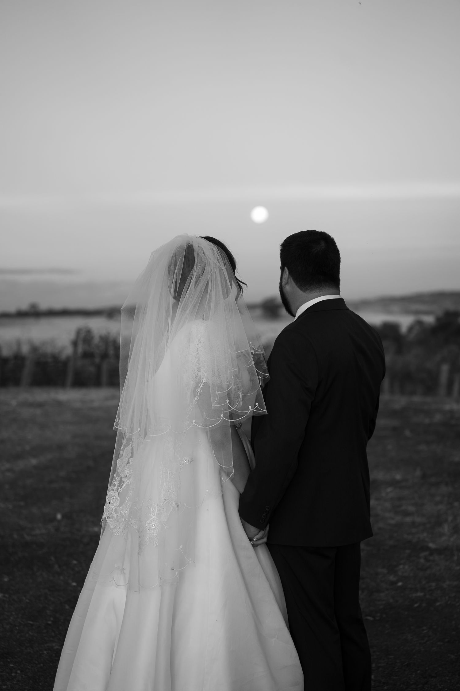 A silhouetted couple in wedding attire watches the sunset together on their special day.