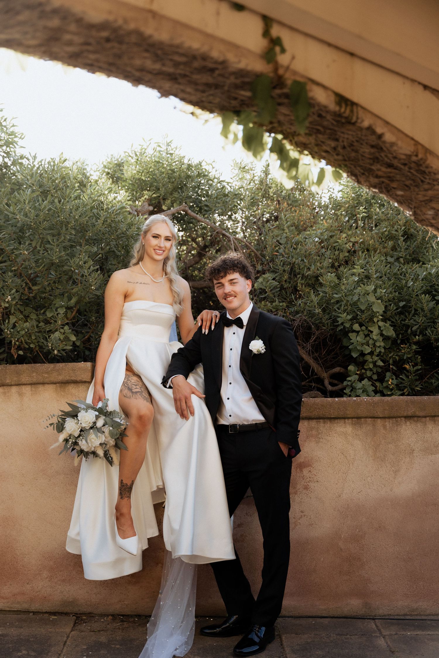 Newlyweds pose together against stone walls and greenery in elegant wedding attire at the alton house pt willunga images by braytmedia