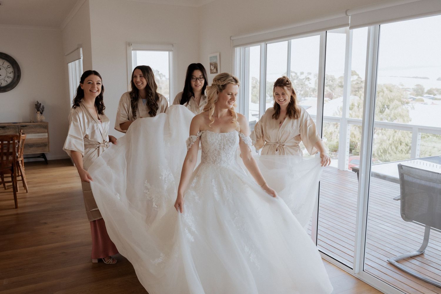 Bridal party celebrating in bright airy room with large windows and ocean views. captured by braytmedia