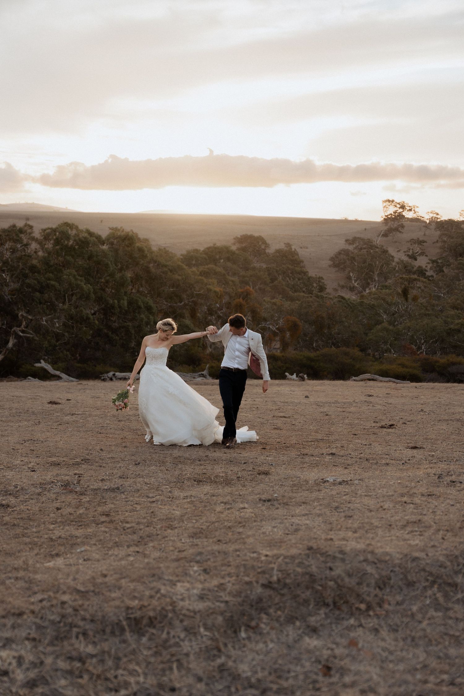 Newlyweds walk together across a scenic hilltop at dusk.