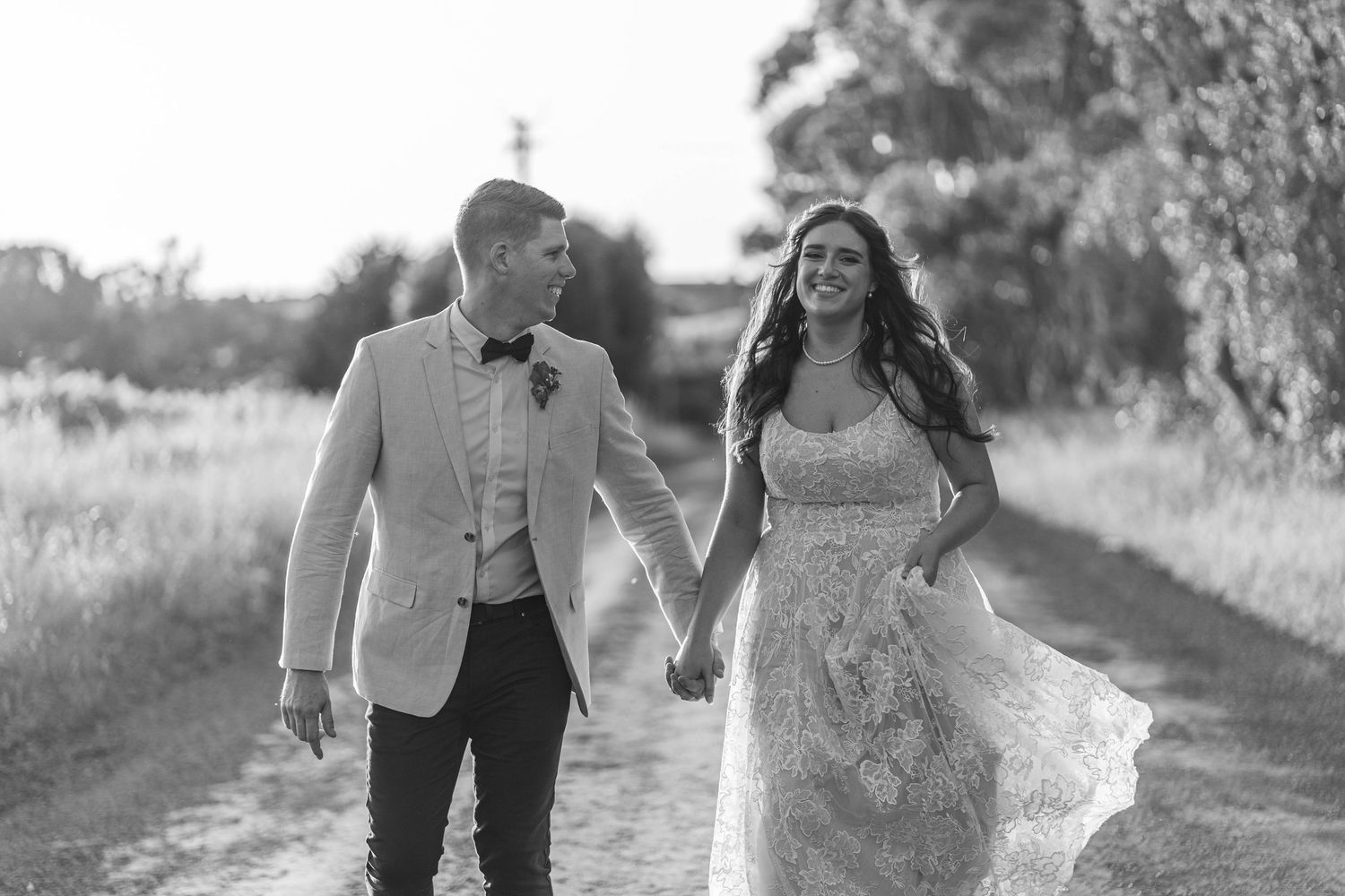 Joyful wedding couple sharing a candid moment on a tree-lined path.