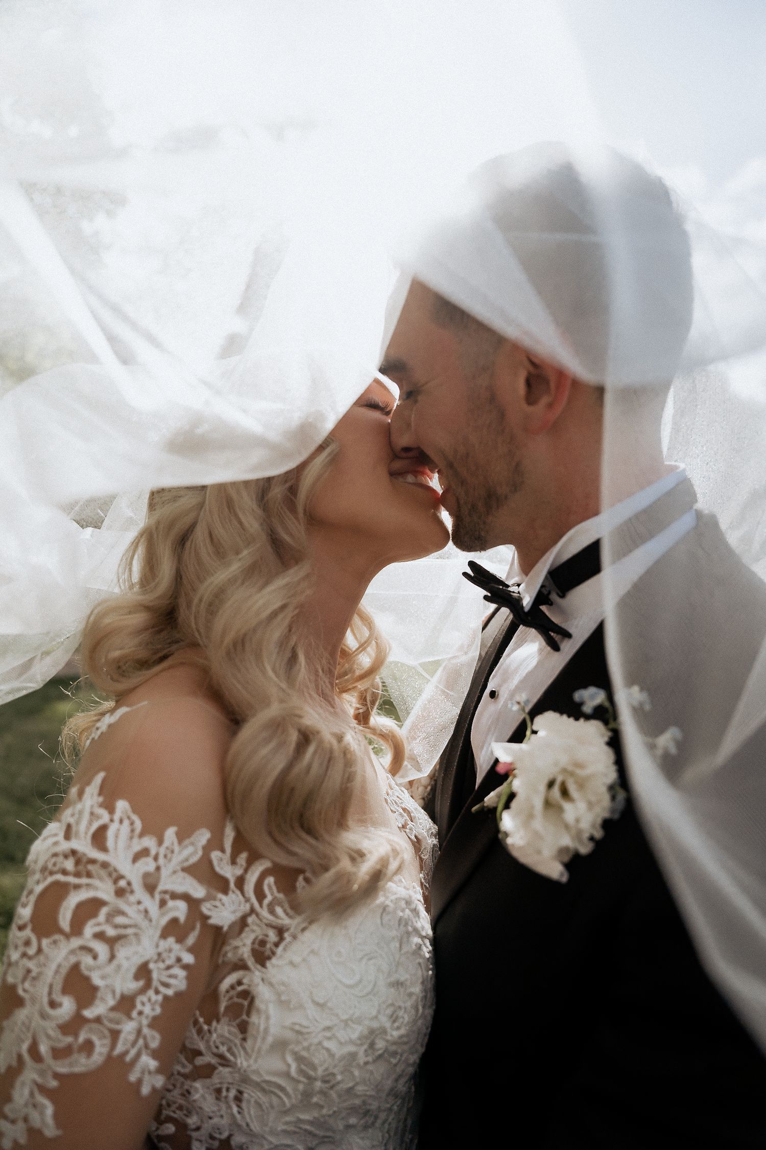 A bride and groom share a romantic kiss beneath a flowing white veil on their wedding day at Carrick Hill by Braytmedia