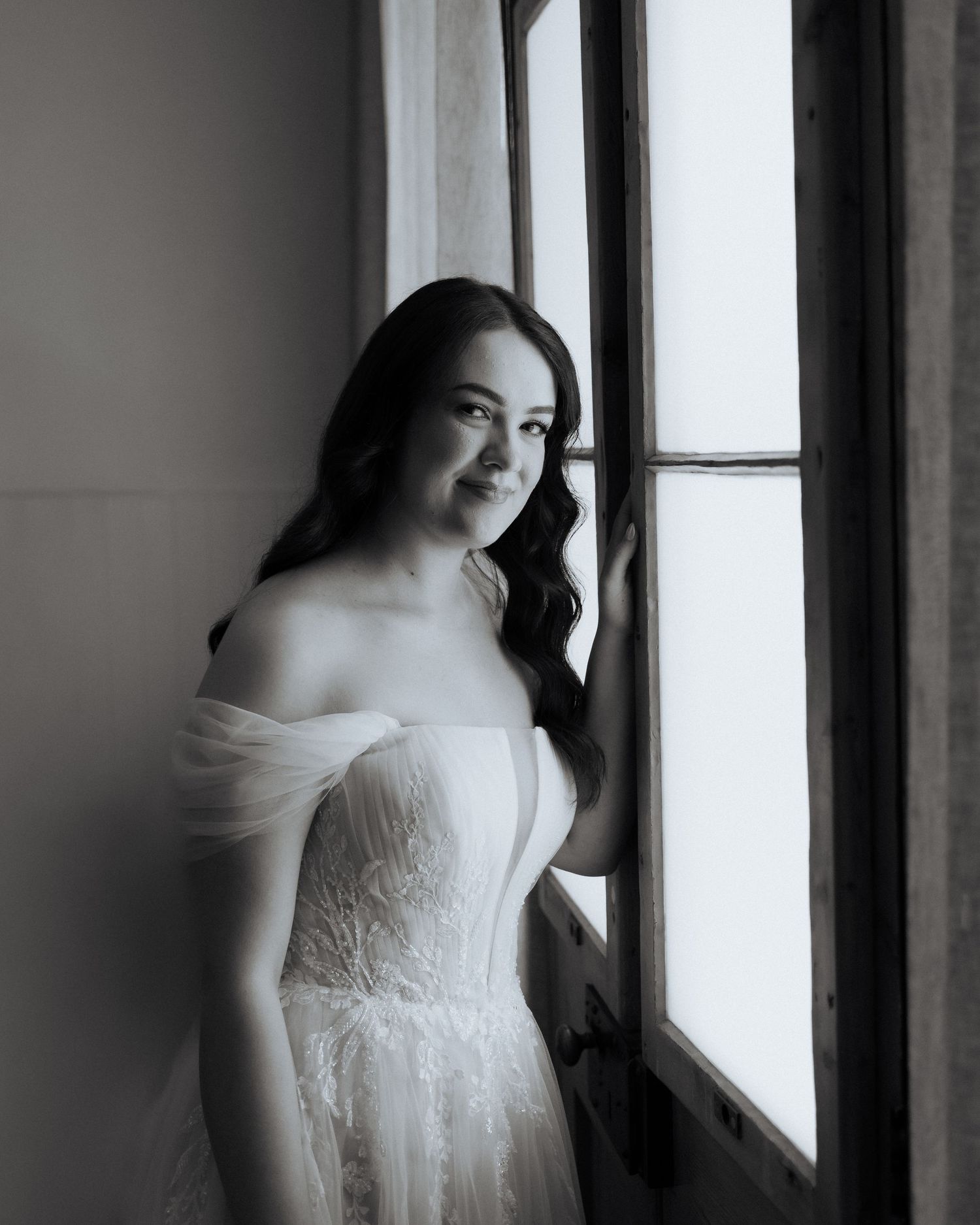 A series of romantic black and white bridal portraits by a window showing an elegant lace wedding dress.