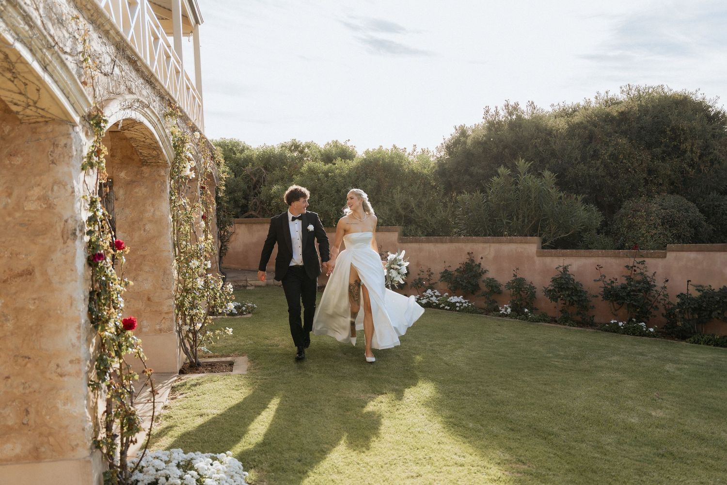 A couple walks down a tree-lined path during a romantic outdoor wedding ceremony at sunset.