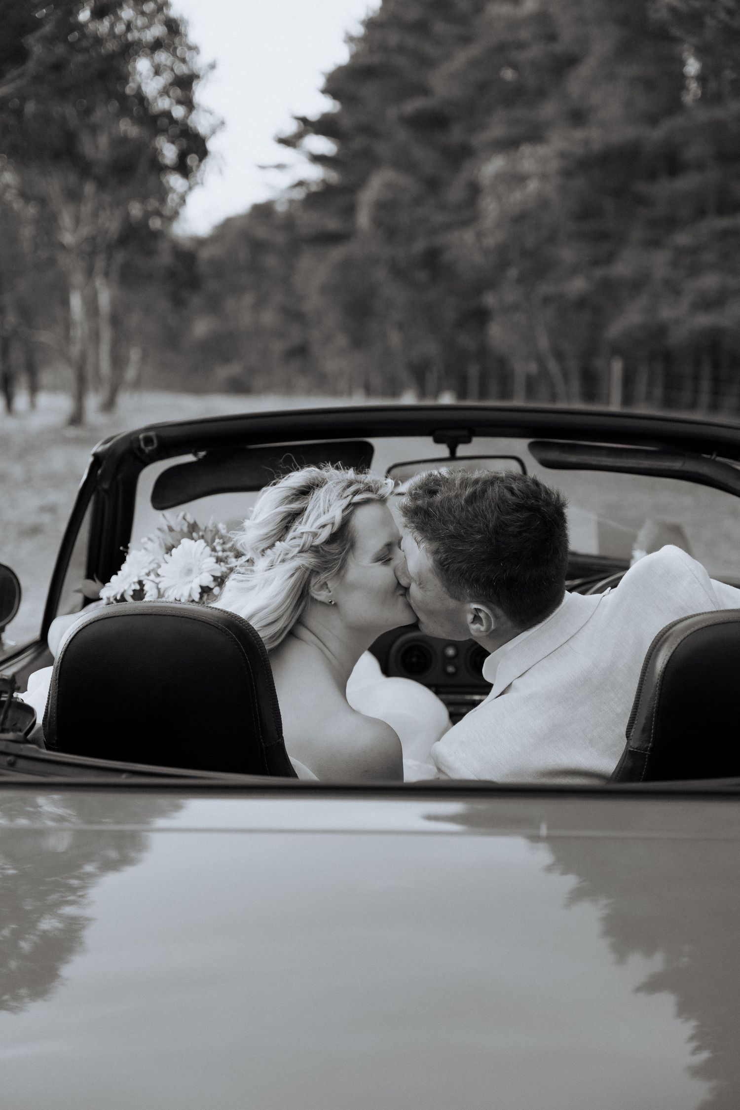 A romantic moment captured in black and white of a couple kissing in a convertible car surrounded by trees. adelaide wedding photography