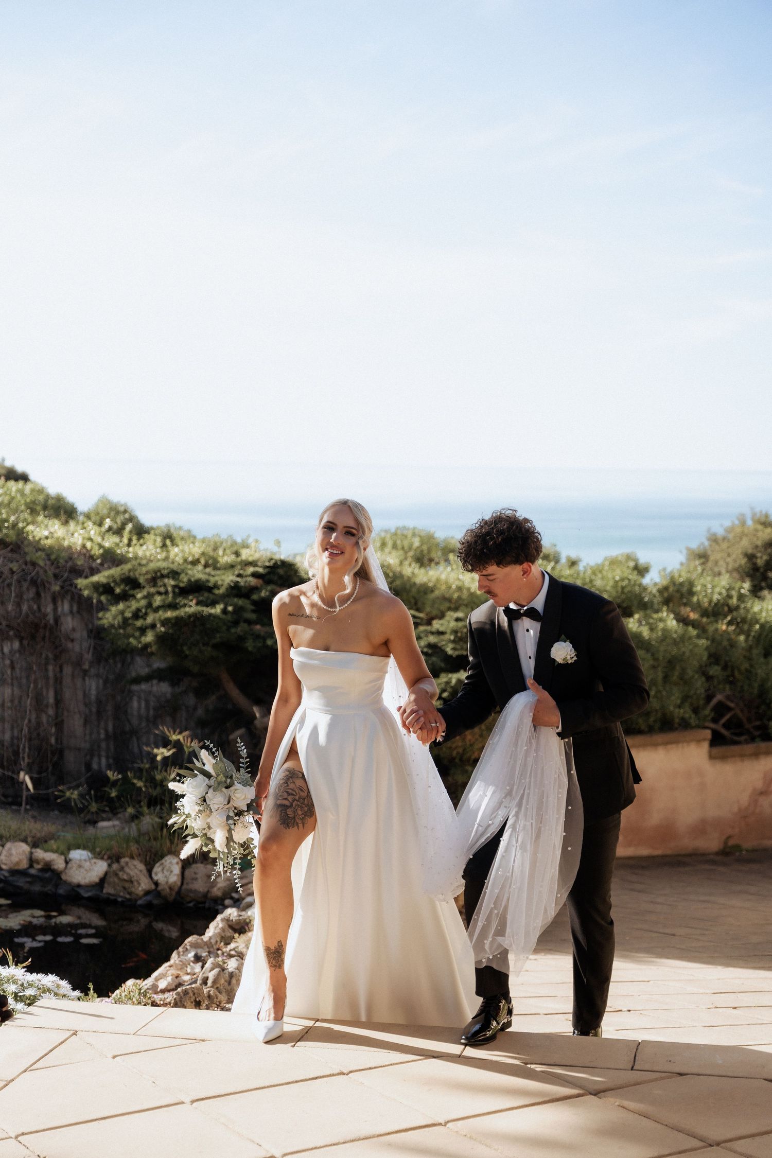 Wedding party walks along a scenic outdoor terrace with ocean views in the background alton house by braytmedia