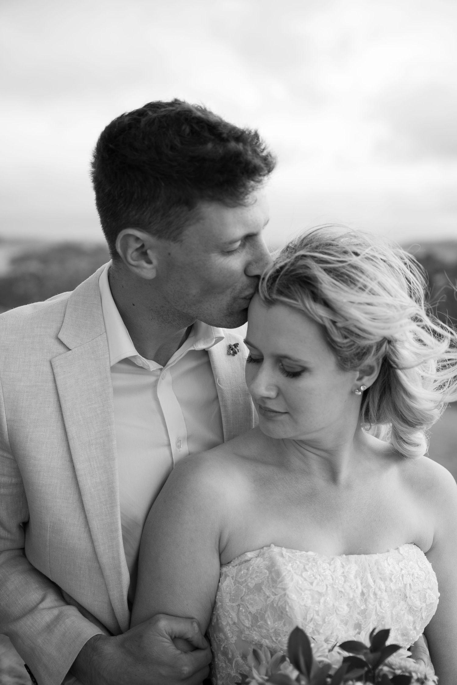 Romantic black and white portrait of newlyweds against cloudy sky.