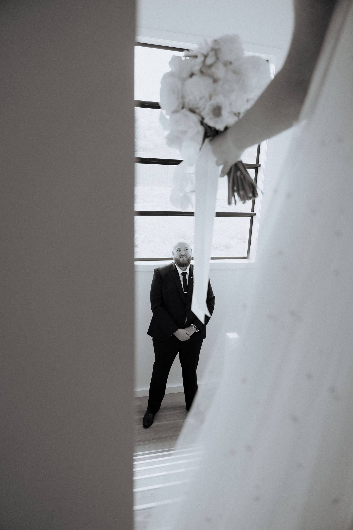 A black and white wedding photo showing a figure in a suit viewed through a doorway with white floral decorations.Lot100 wedding venue image