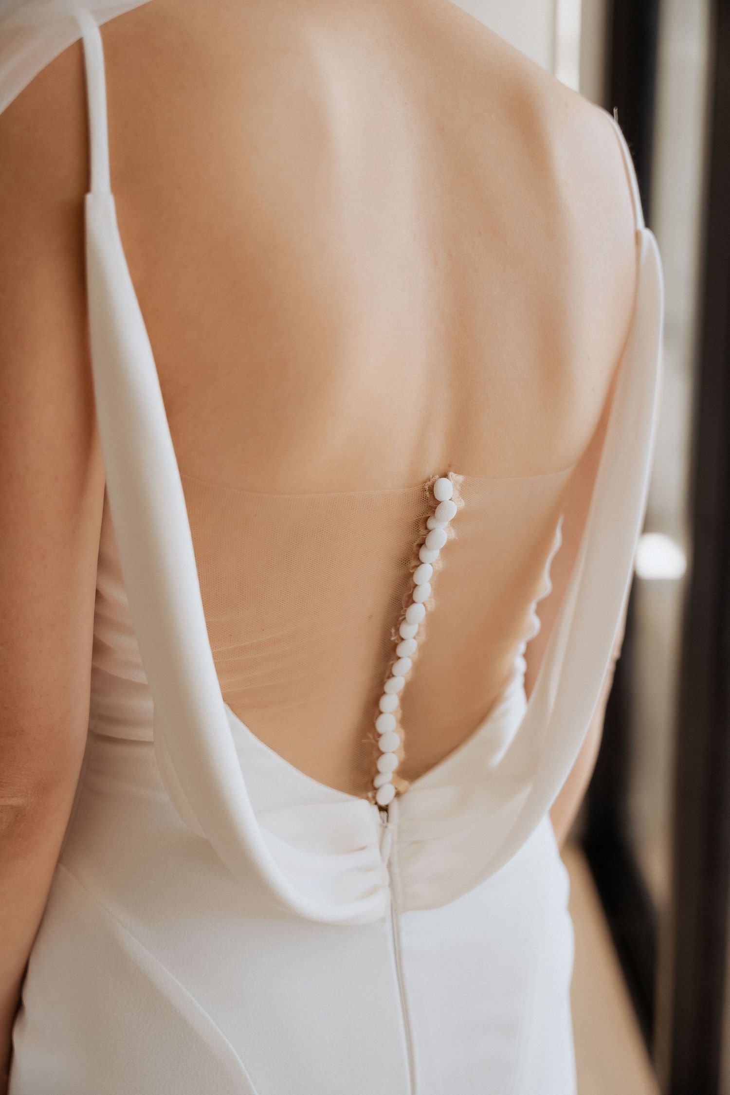 Close-up of elegant white wedding dress with pearl button details on the back.