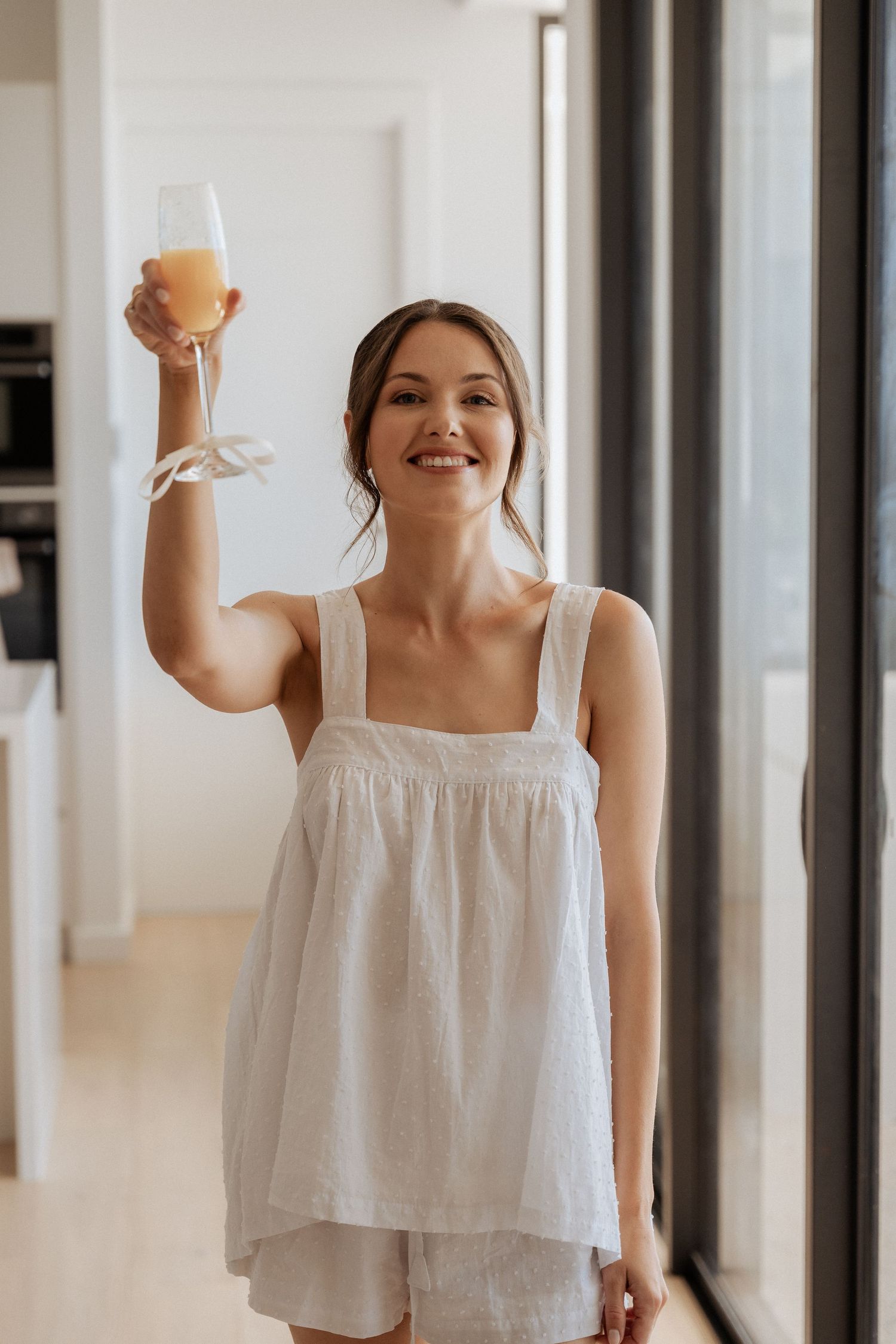 Person in white summer dress holding up drinks while smiling.