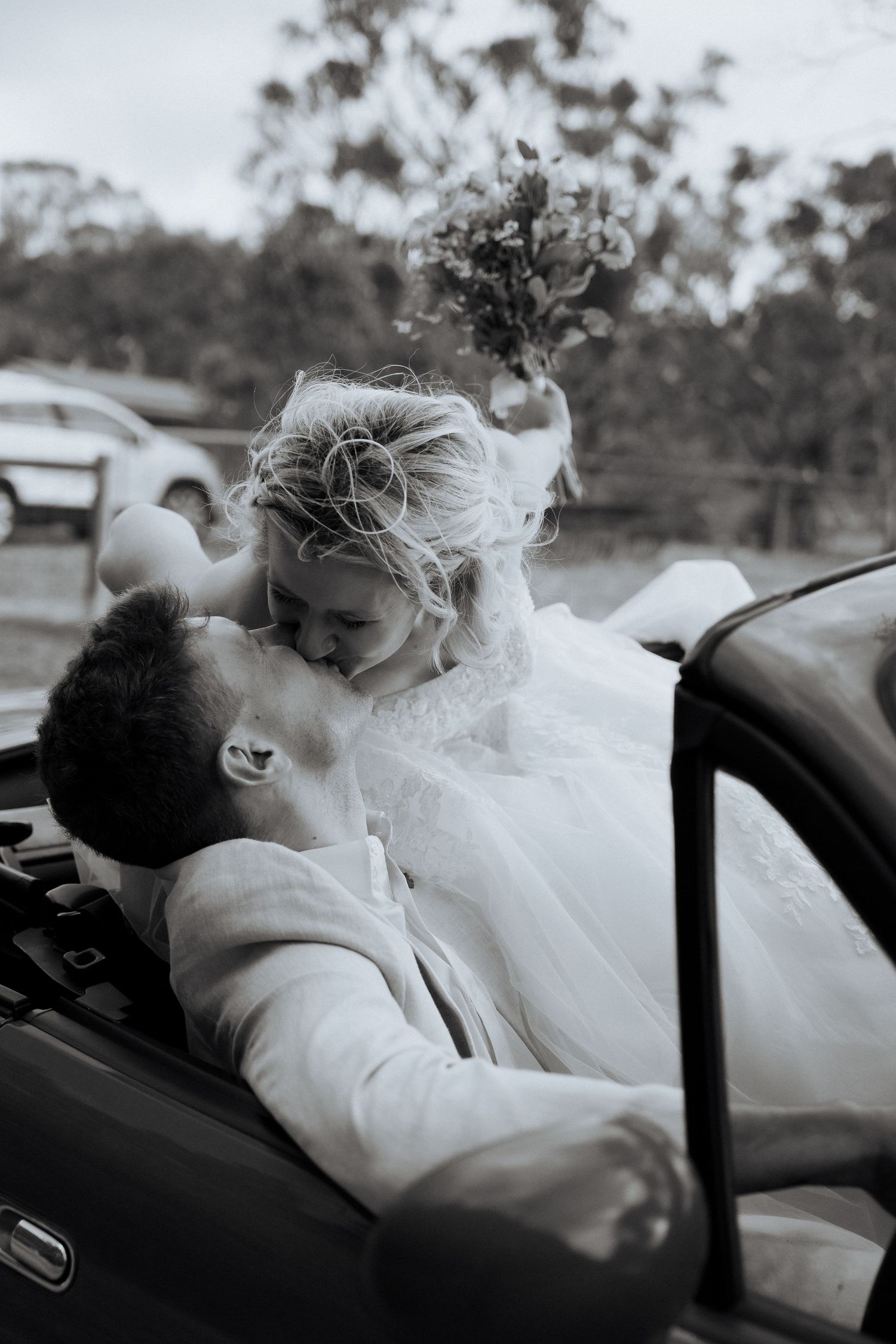 Intimate black and white moment of newlyweds in a convertible car.