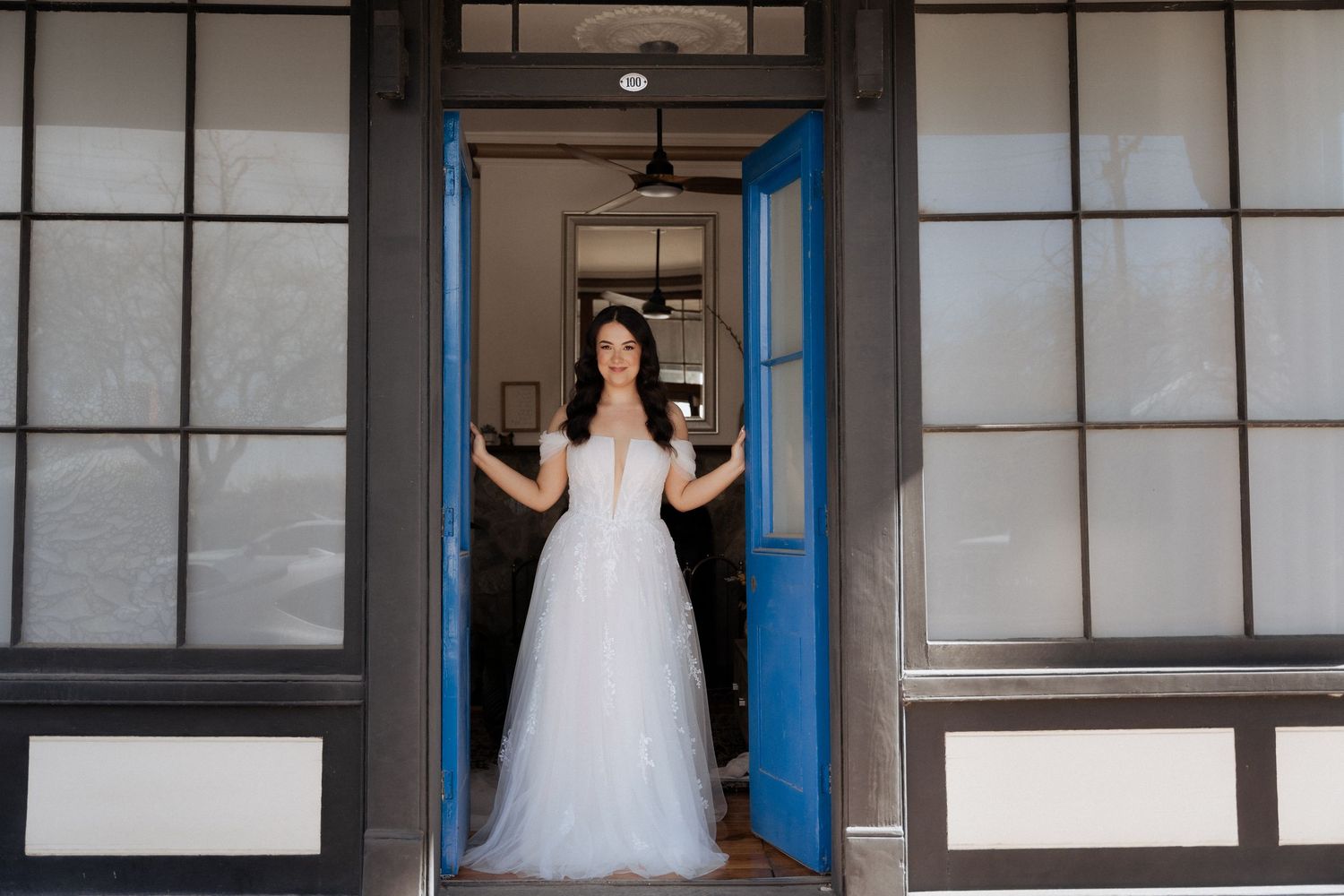 A series of bridal gowns displayed in a row of changing room stalls with blue trim and white walls.