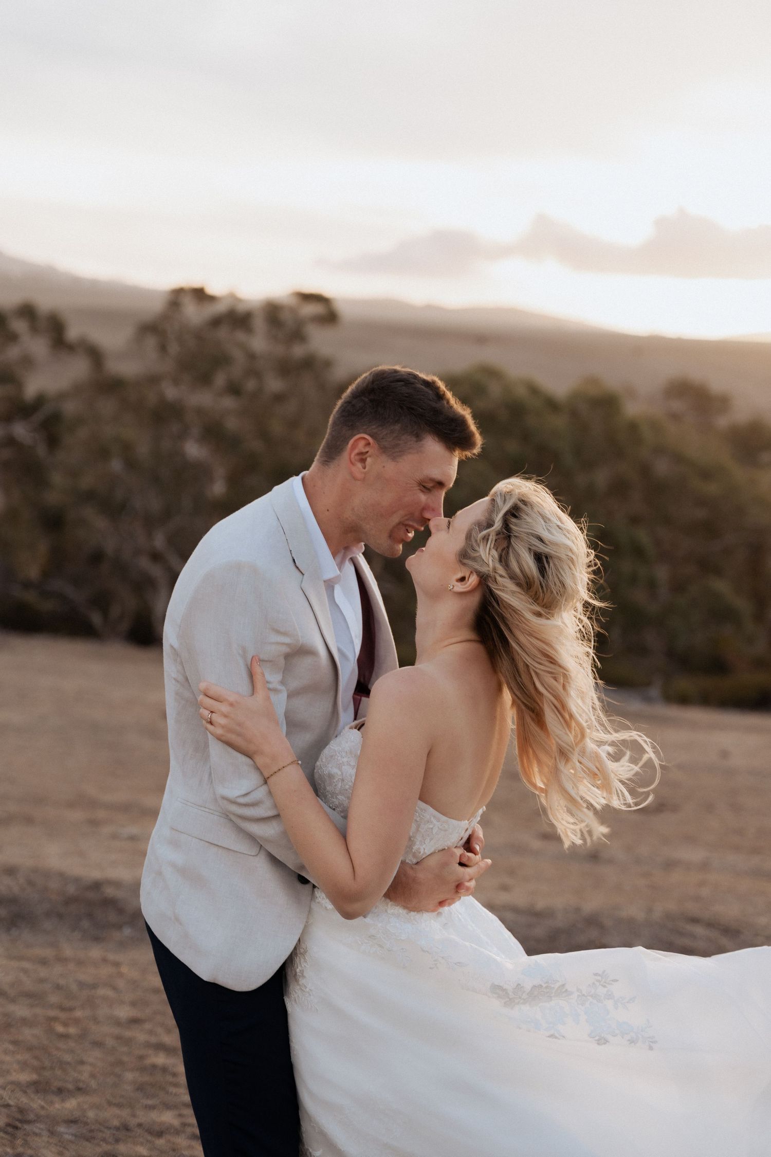 Couple in wedding attire embrace while sharing an intimate moment during golden hour.