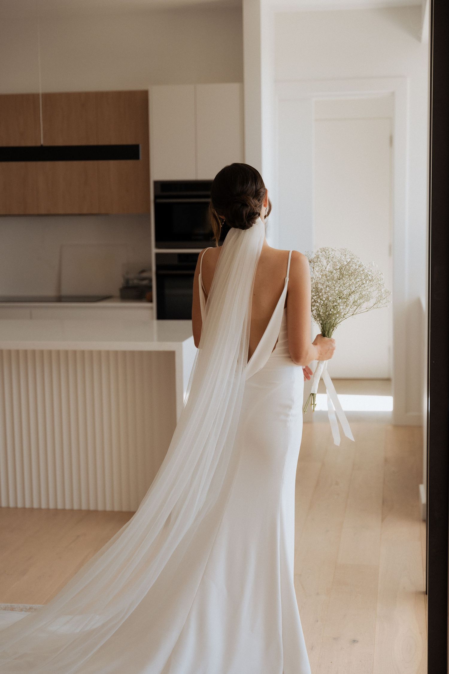 A flowing white wedding dress with a long train captured in an elegant minimalist interior.