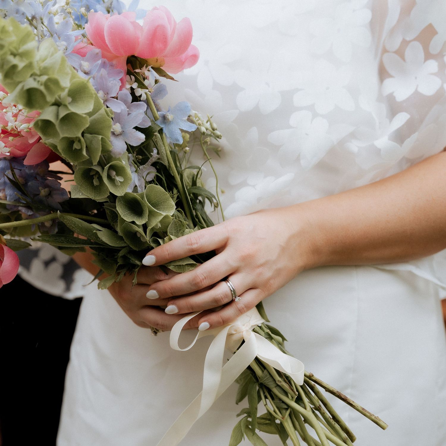 A close-up of a bride holding a colorful bouquet of pink and blue flowers with a wedding ring by Braytmedia Ivybrook farm