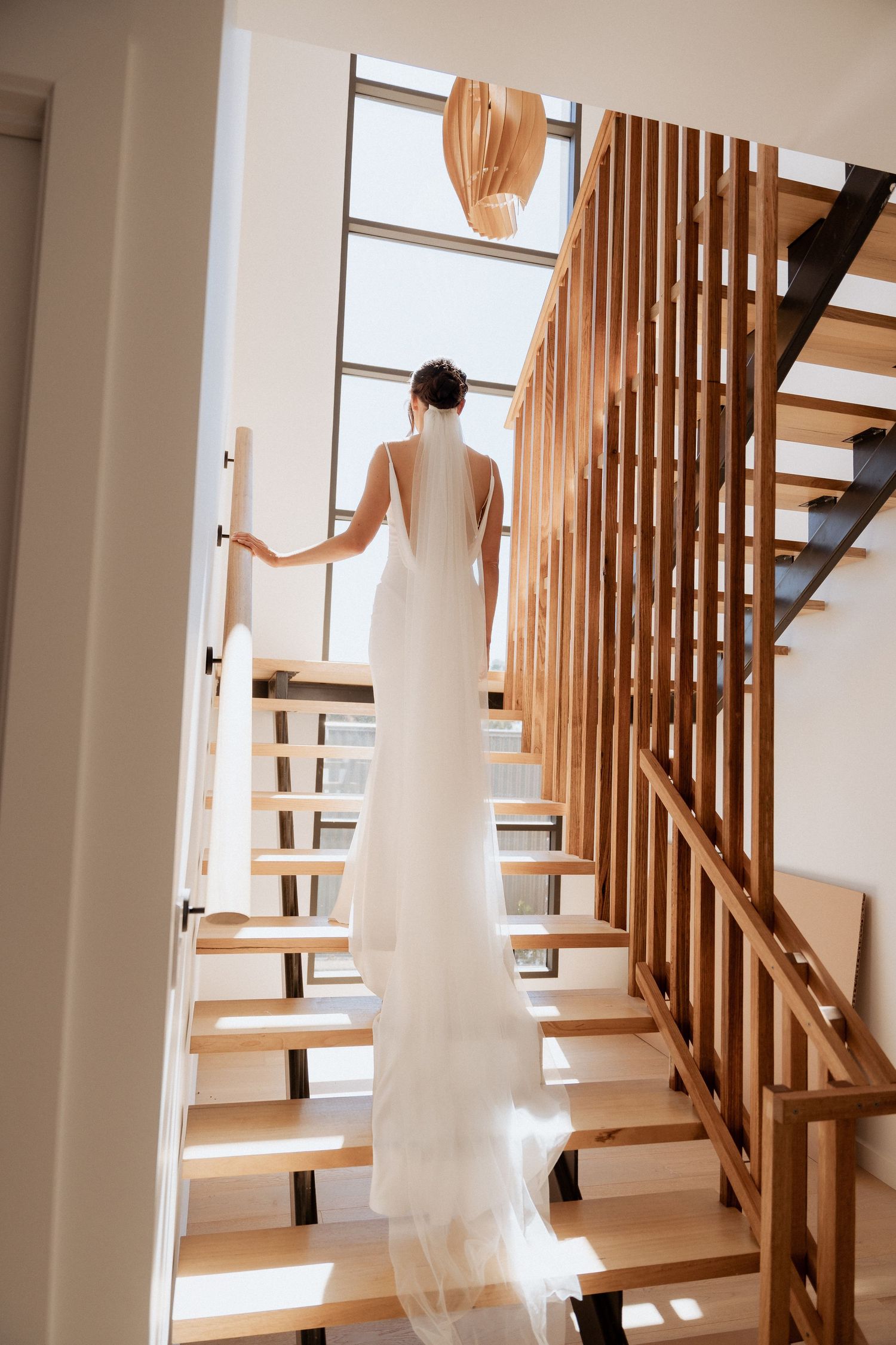 White wedding dress flowing down wooden staircase in modern interior with natural light. captured by braytmedia