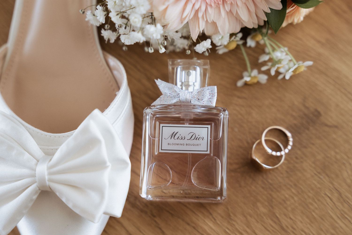 Wedding details including perfume bottles, white bow ties, and delicate pink flowers on wooden surface.