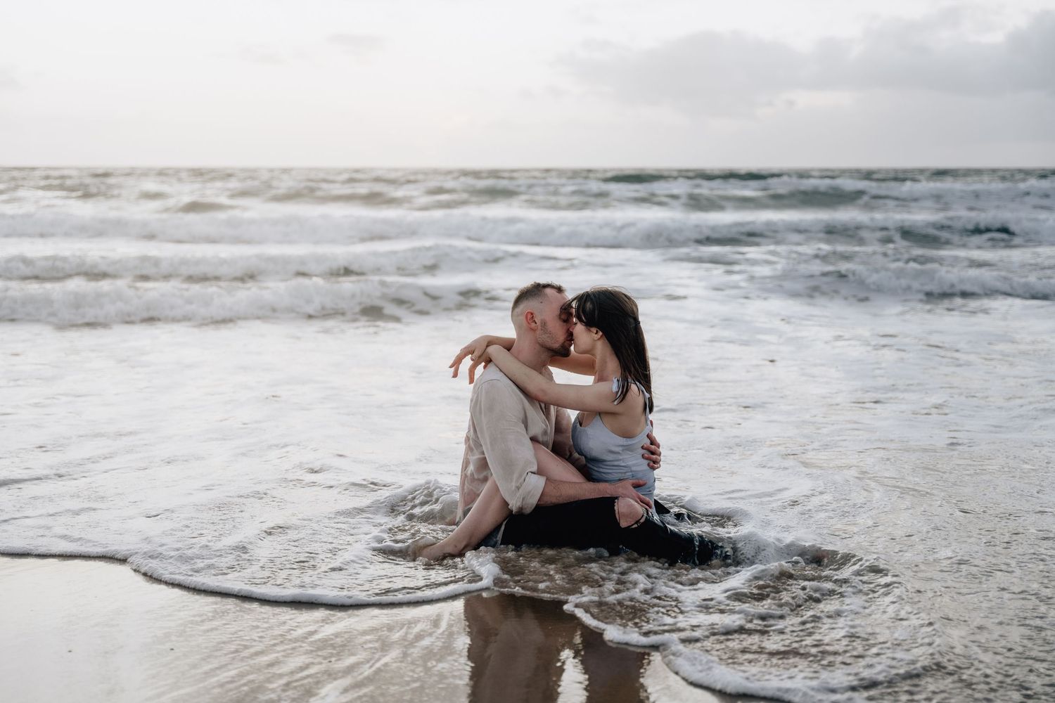Waves crash around a couple during their romantic beach photo session.