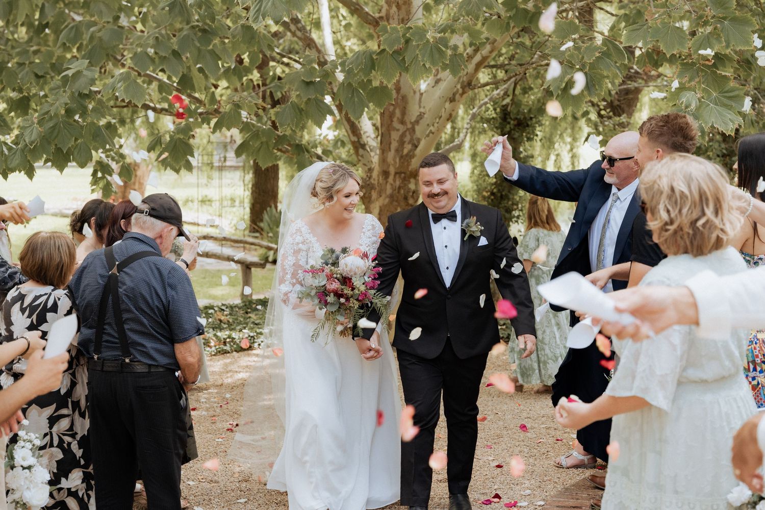Wedding celebration scene with guests throwing confetti in an outdoor garden setting.