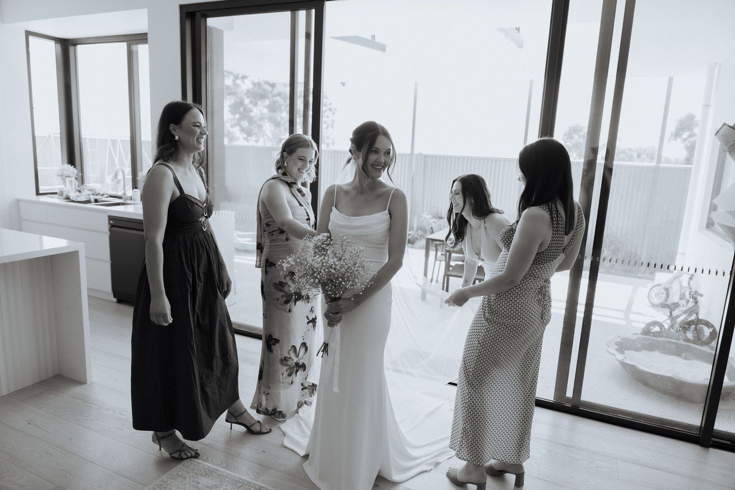 Wedding party members in light colored dresses gathered in a bright modern space.