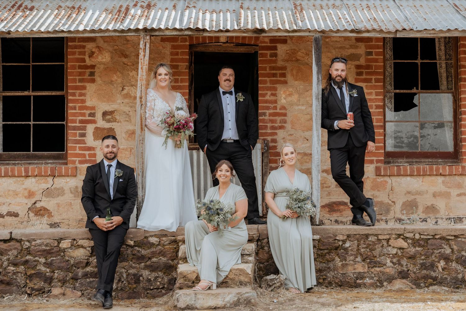 Wedding group photos taken against a rustic brick building with stone foundation.