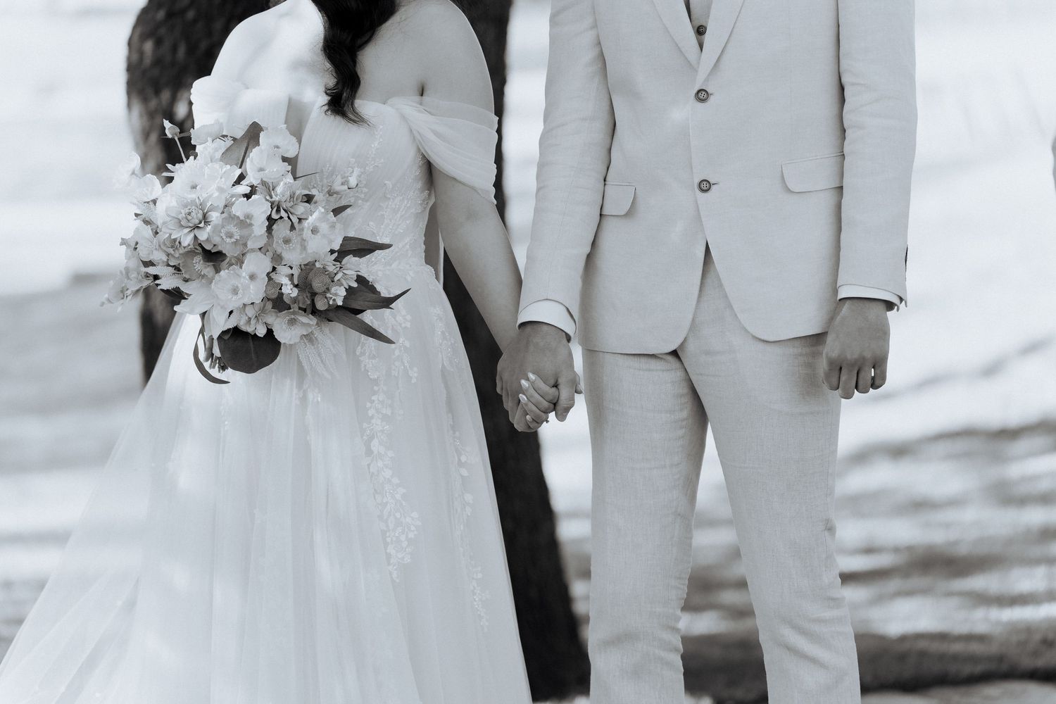 Wedding party in light colored suits and dresses poses together on a beach at sunset.
