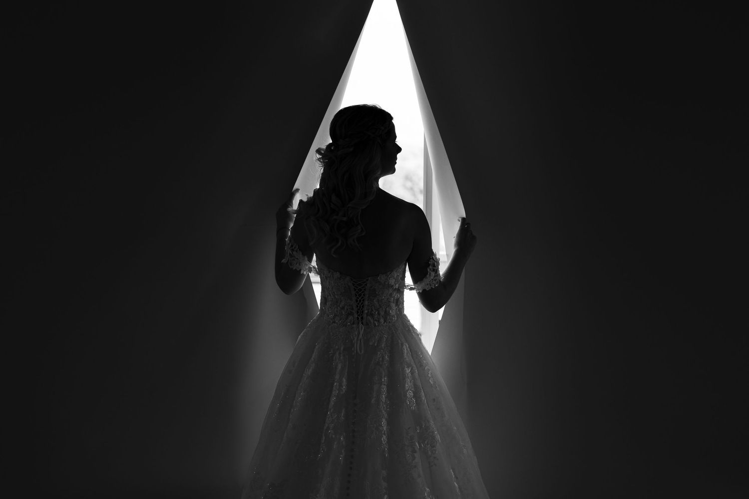 Dramatic silhouette of a wedding dress against dark background.