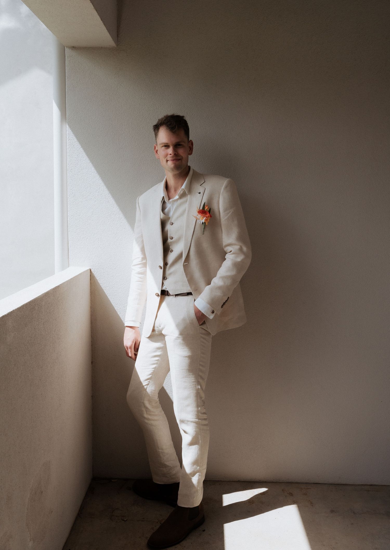 Figure in white suit strikes dynamic poses against minimalist wall backdrop creating artistic fashion portraits in natural light.