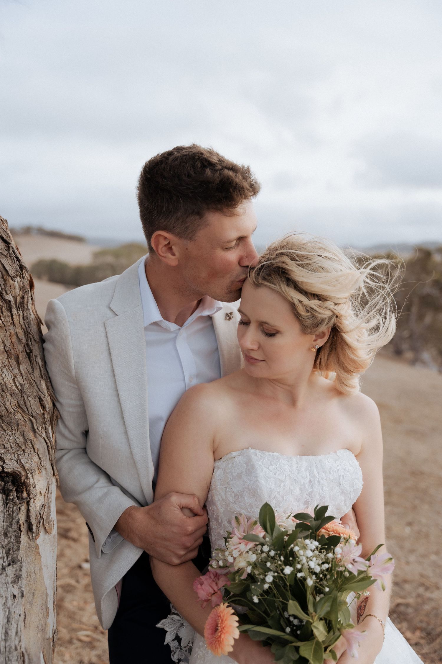 Intimate wedding portraits captured in a natural outdoor setting with soft lighting and floral bouquet.