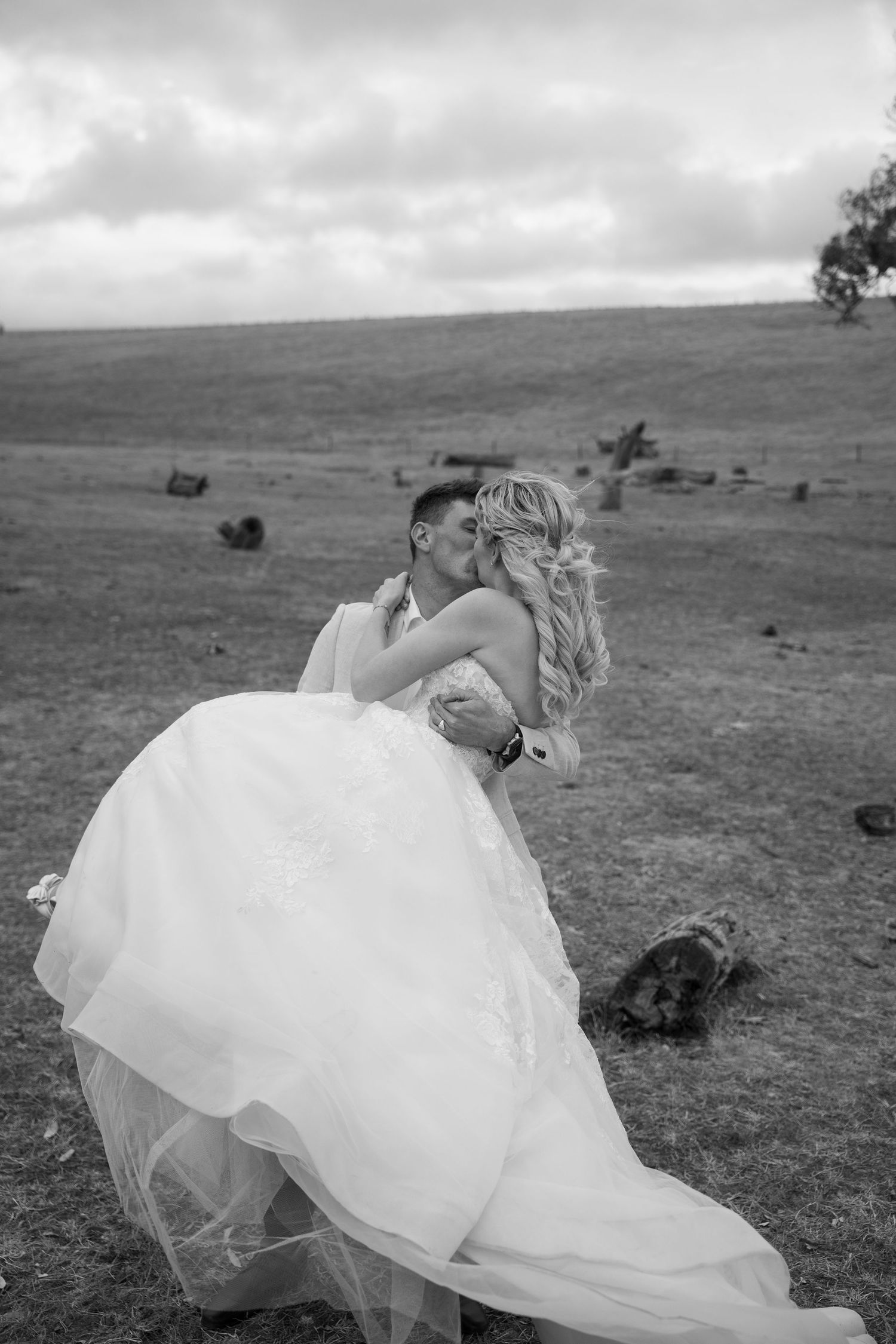 Black and white photo of couple dancing in an open field with flowing wedding dress.