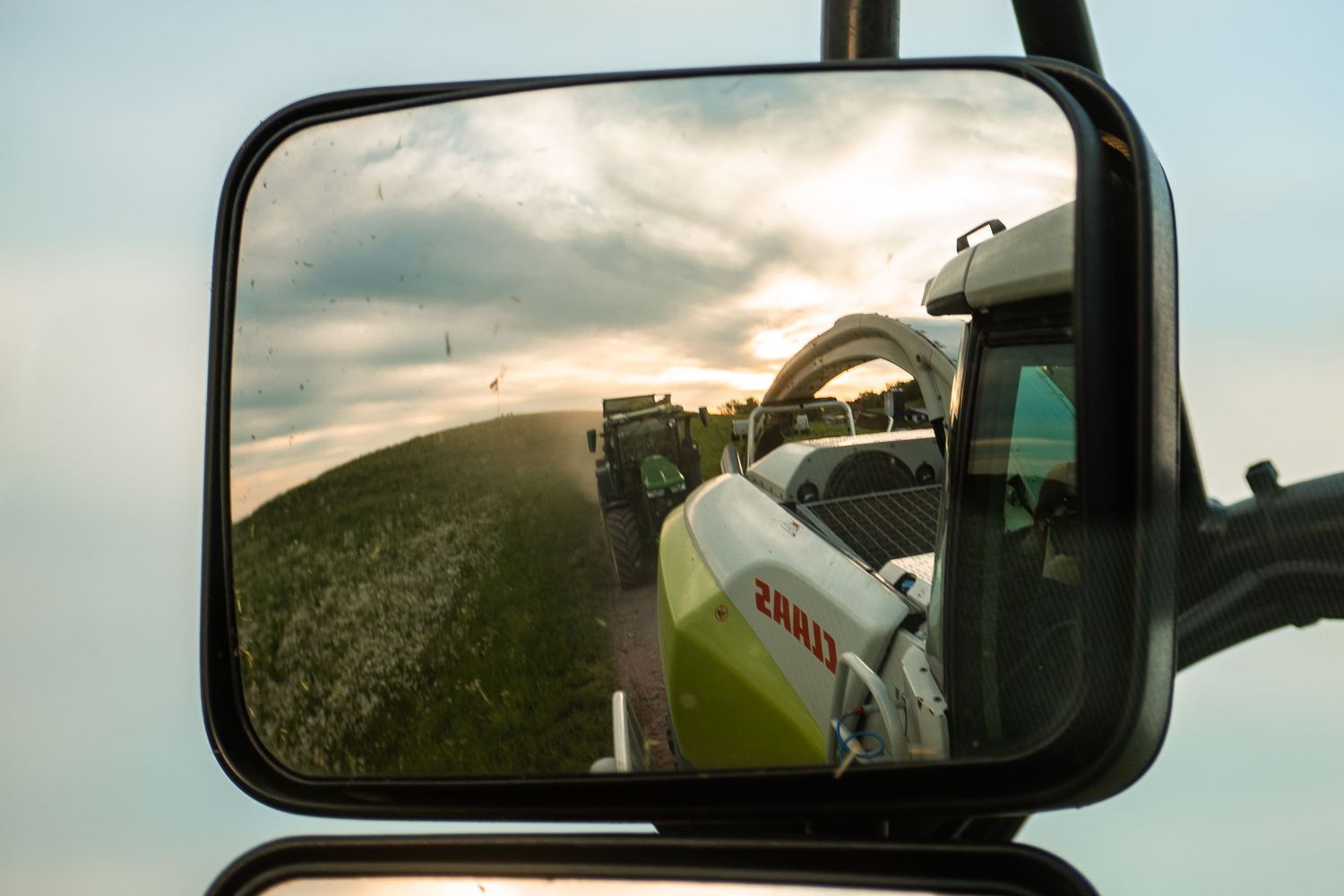 View through vehicle mirrors of farm equipment working in fields.