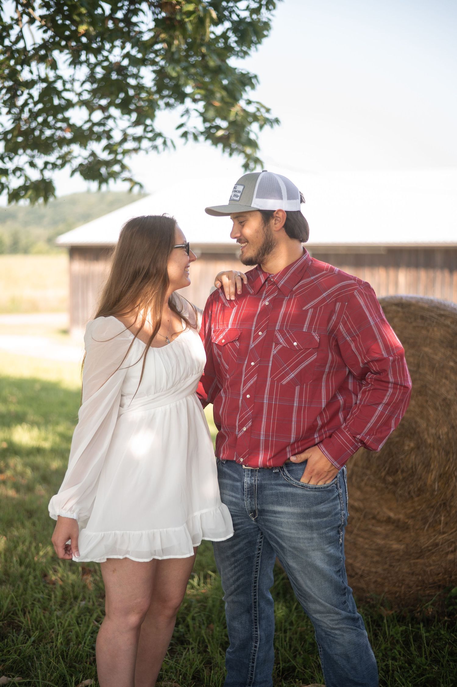 A couple poses together near hay bales in a rustic farm setting.