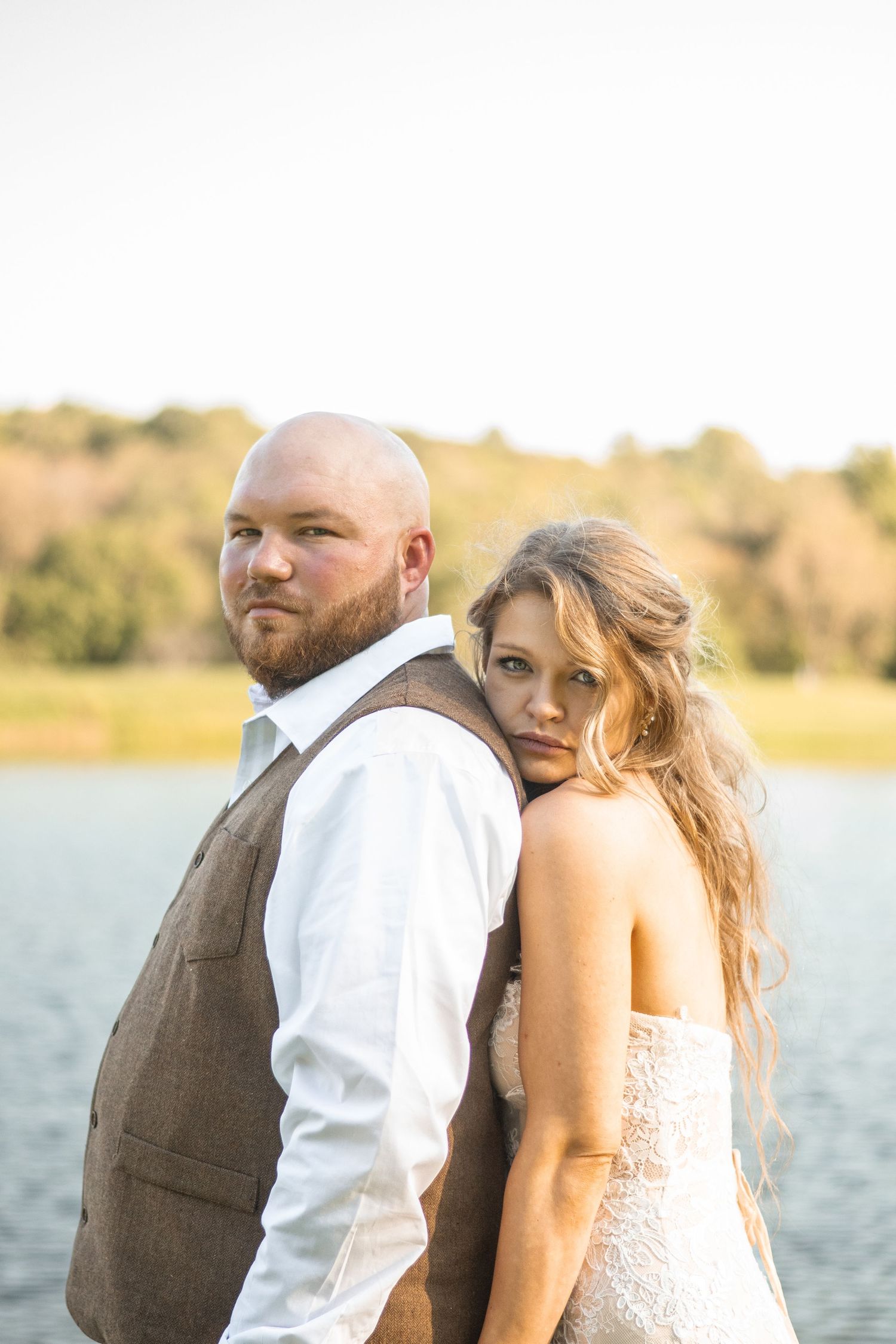 Romantic lakeside moment with a couple in wedding attire silhouetted against golden sunlight.