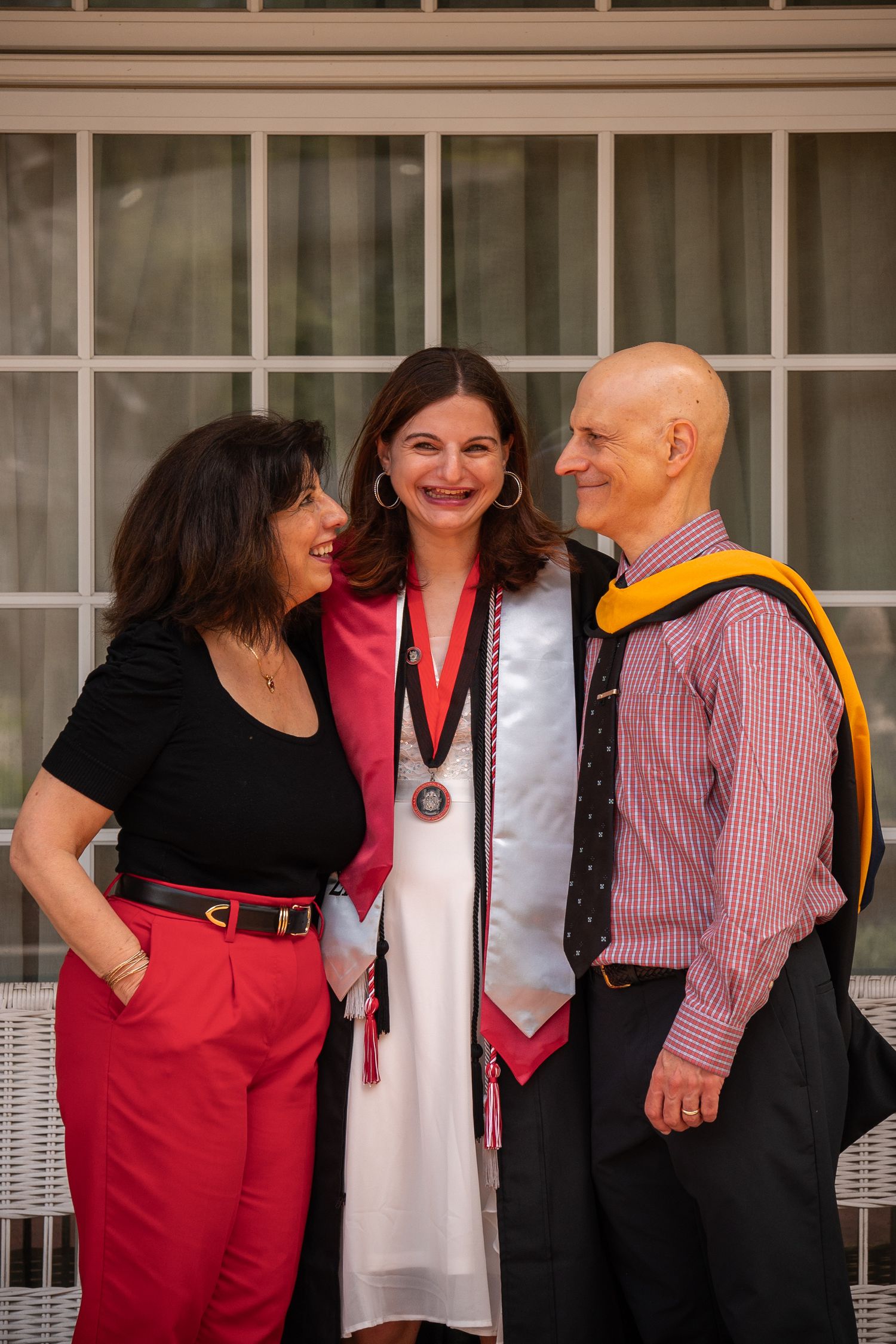 A group of graduates in red and black academic regalia pose together outdoors.