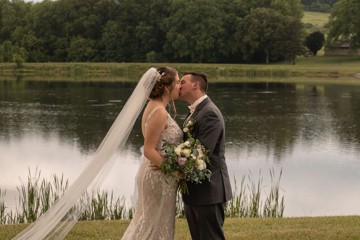 Romantic wedding couple shares tender moments by a serene lake surrounded by lush greenery and cattails.